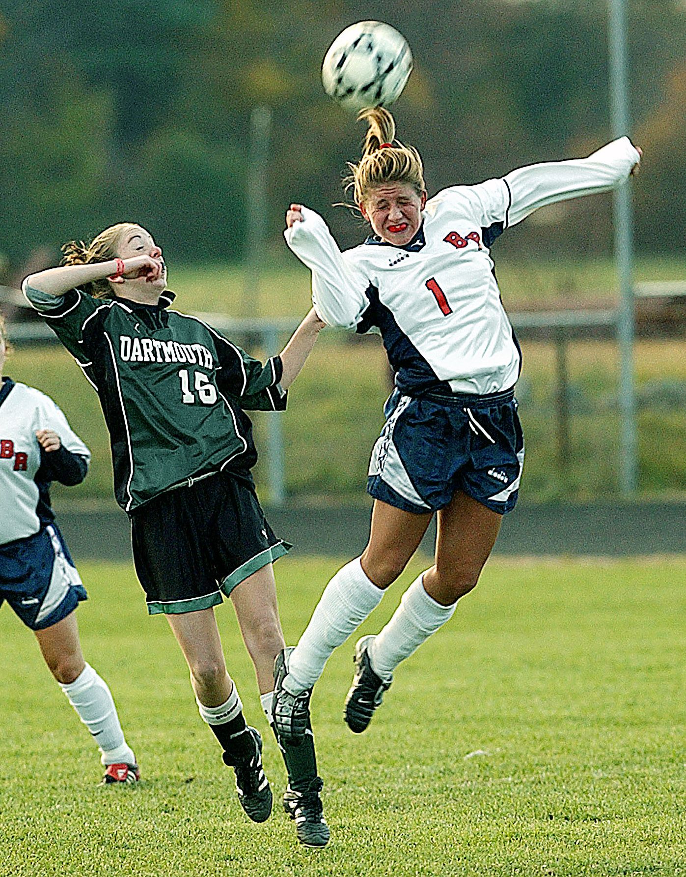 Two female soccer players compete for a header during a match, with a Dartmouth player in green and opponent in white.