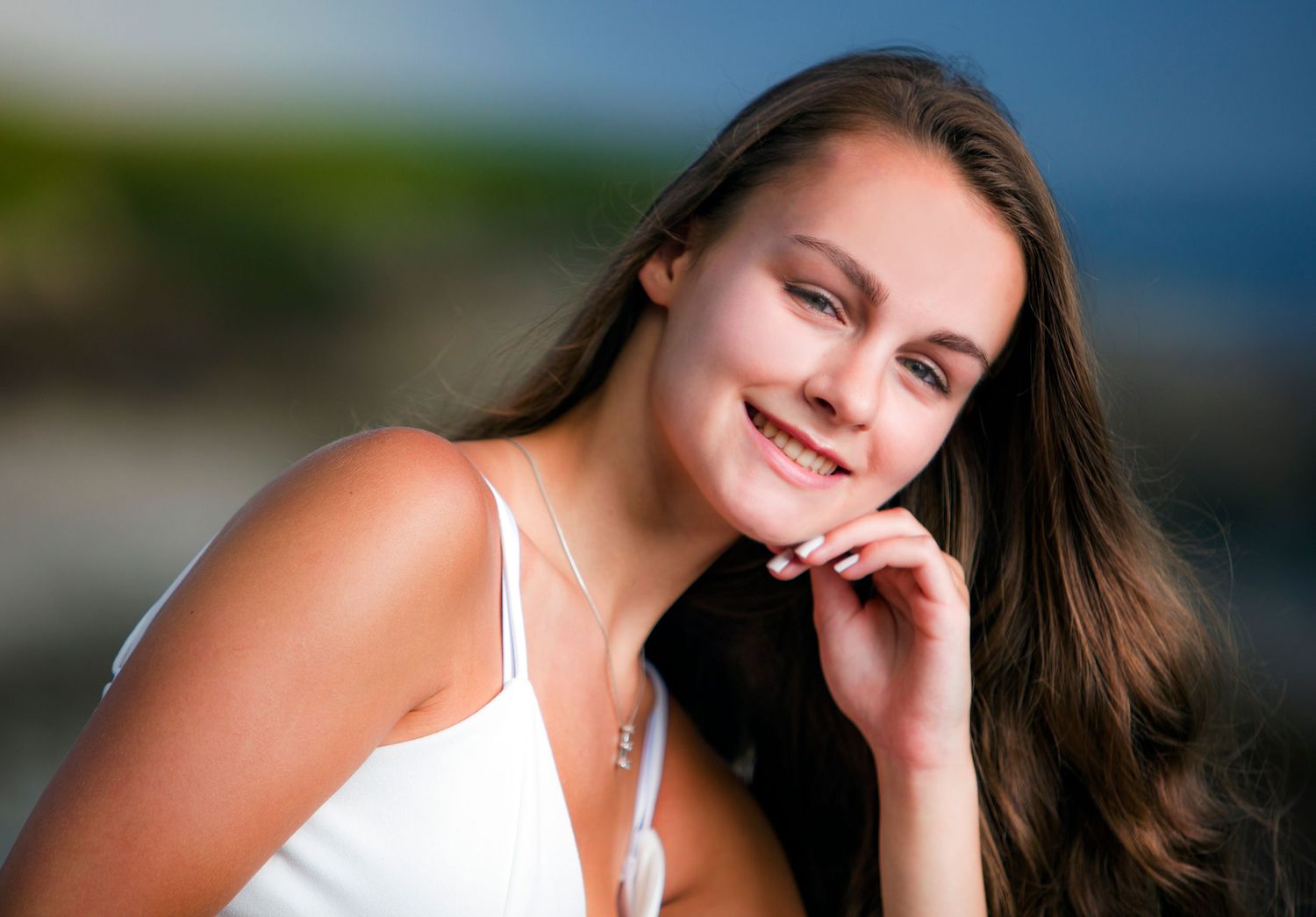 Smiling brunette teen girl in white dress with soft bokeh outdoor background portrait.