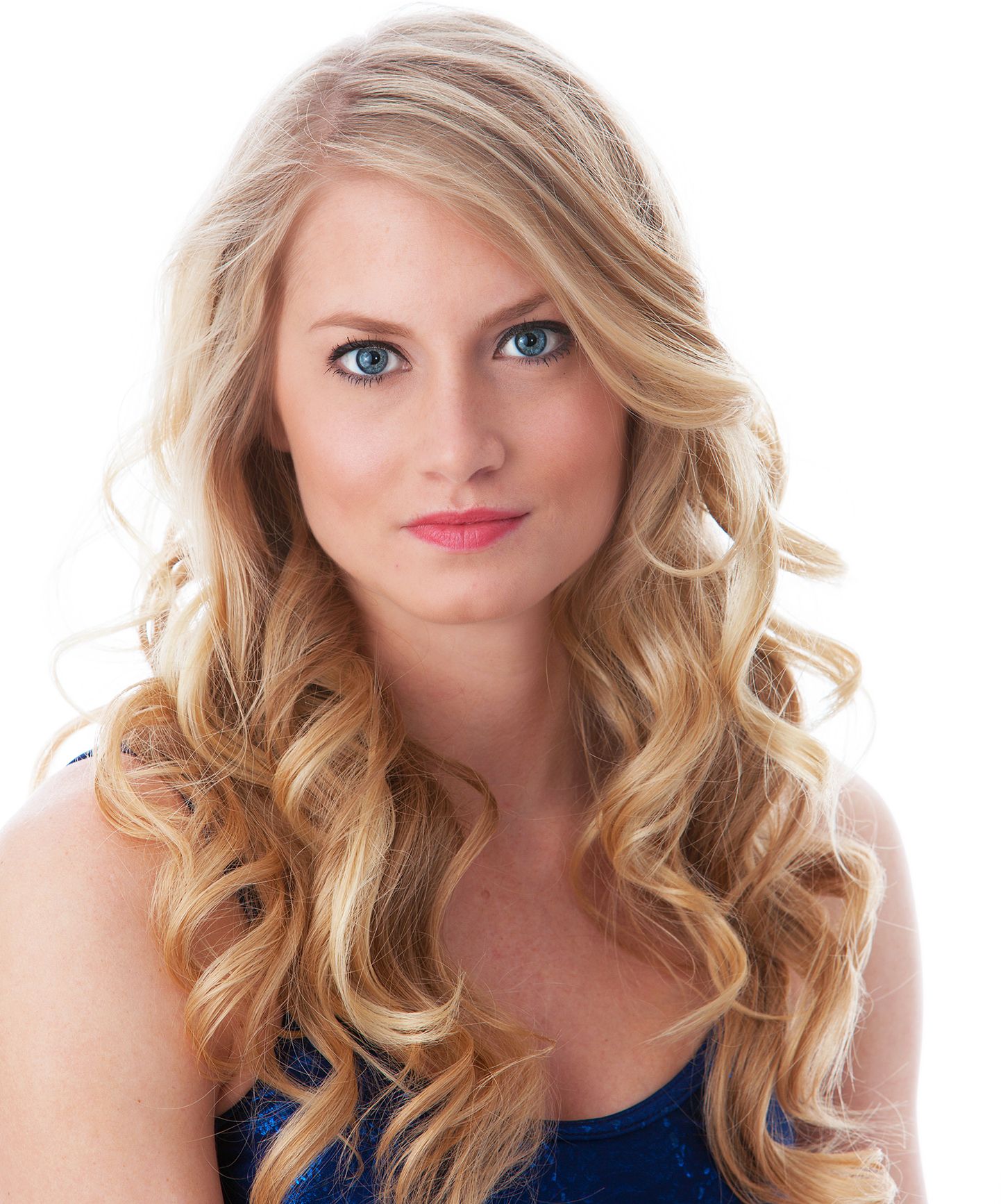 Young woman with long blonde curly hair and blue eyes wearing a blue top against a white background.