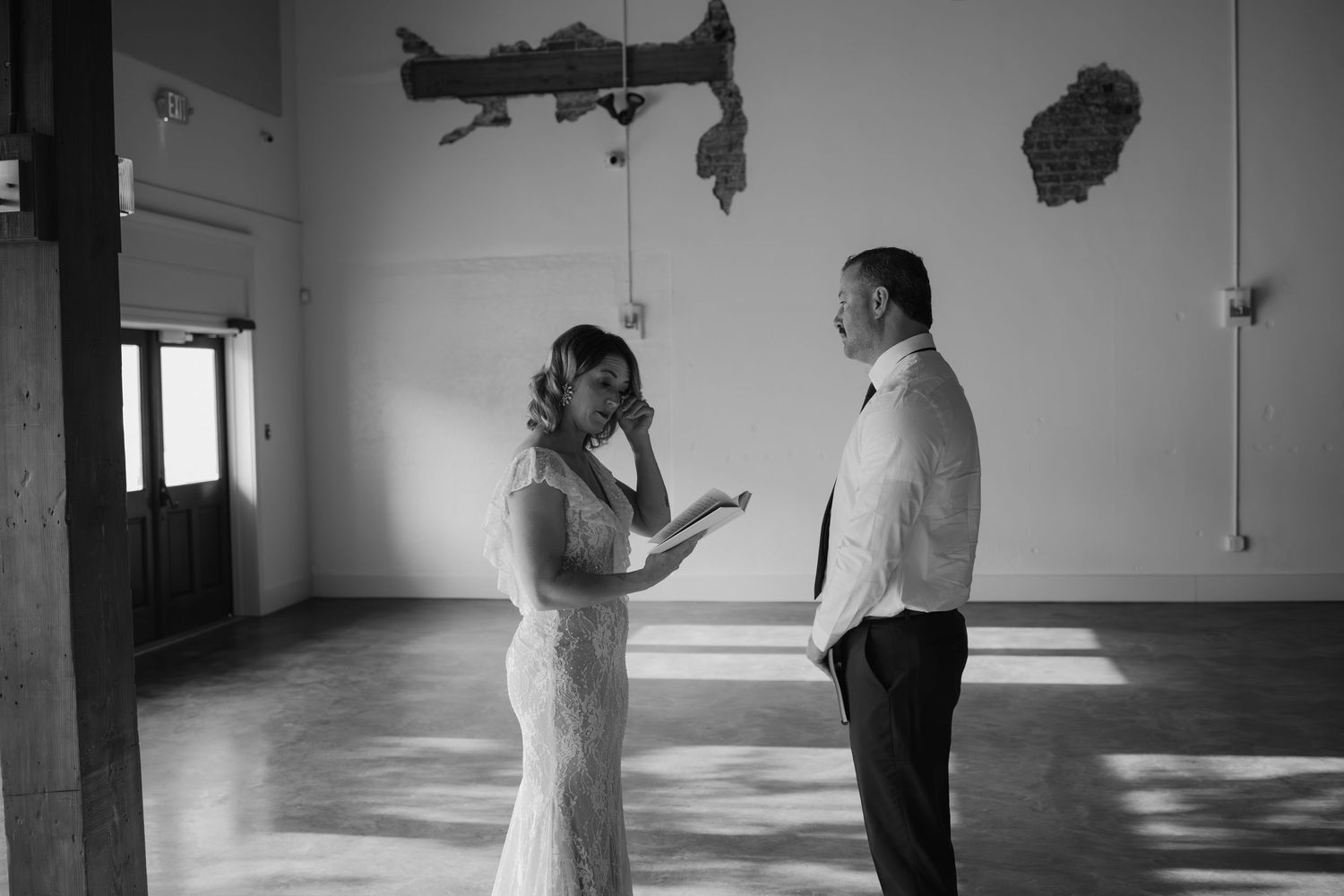 Black and white photo of emotional bride wiping tears during first look with groom indoors.