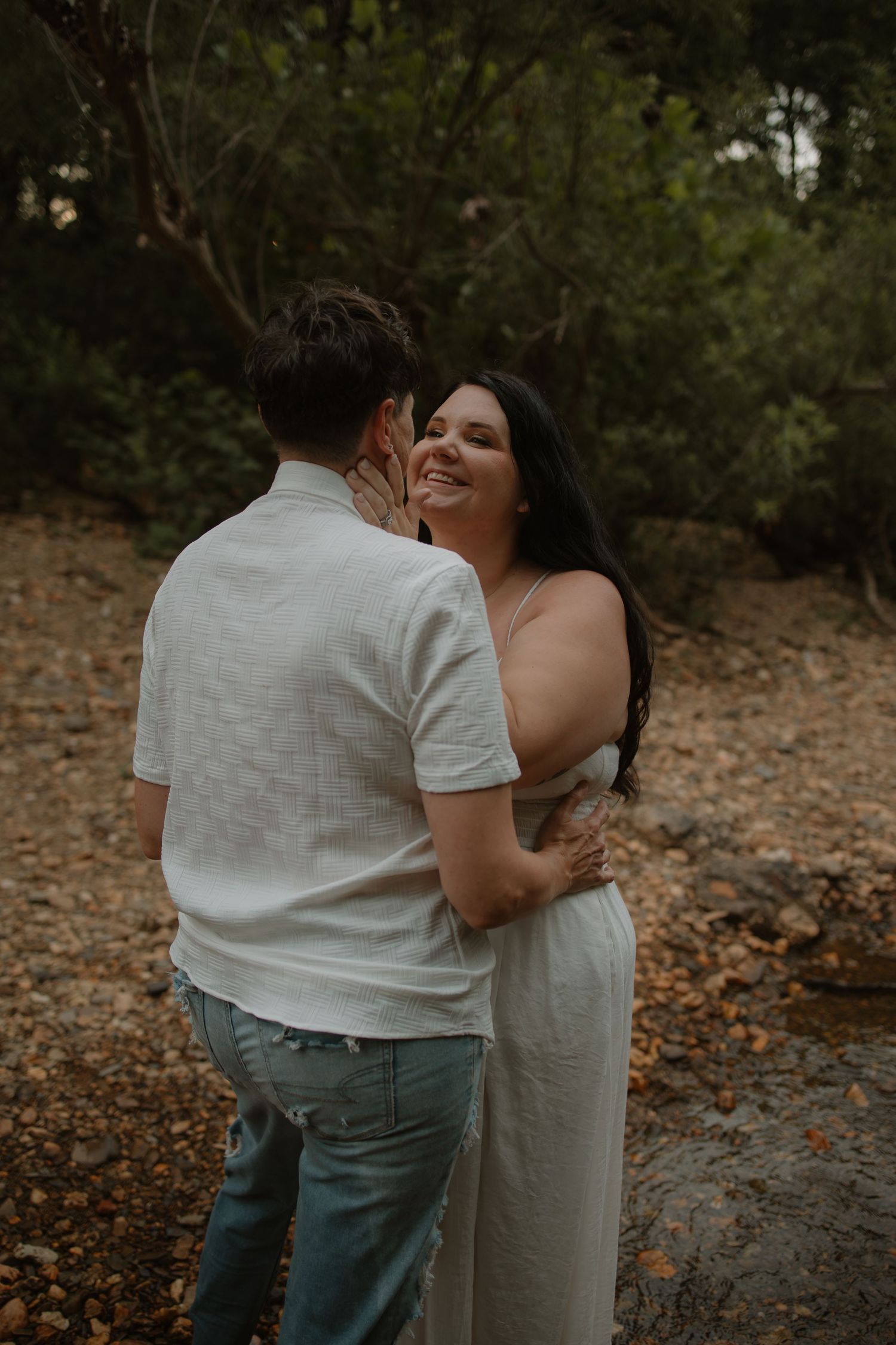 Happy dark-haired woman laughing while embracing partner on a rocky outdoor terrain.