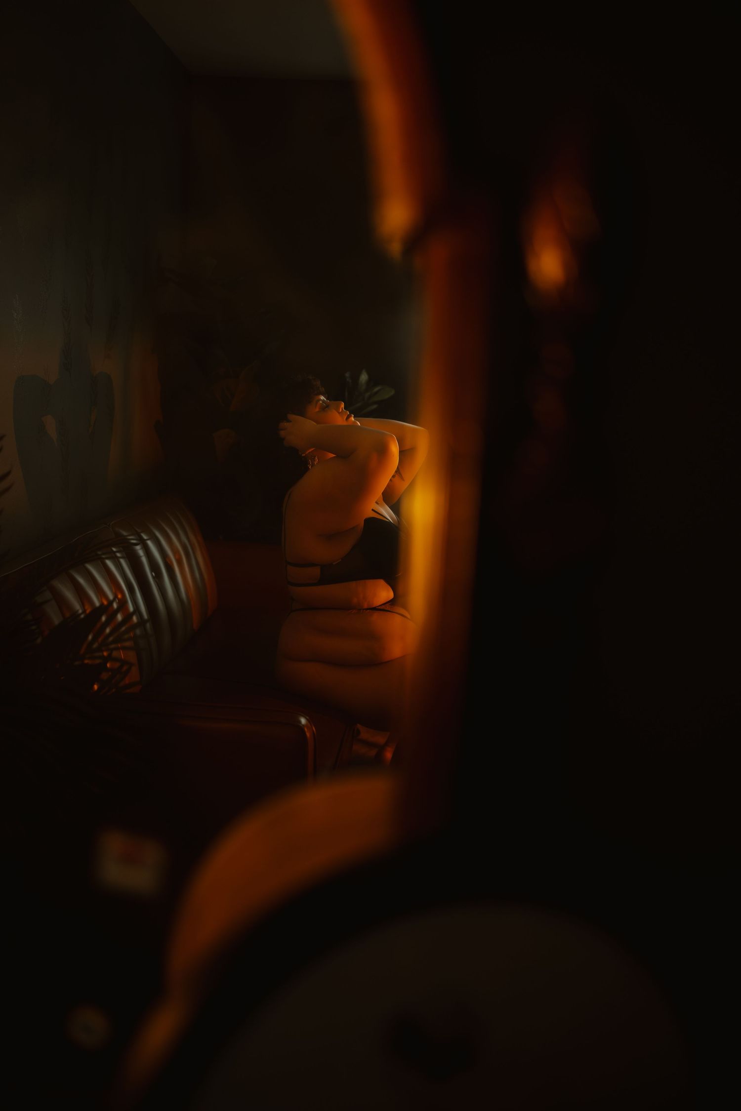 Dark moody mirror reflection showing partial figure in warm candlelight glow.