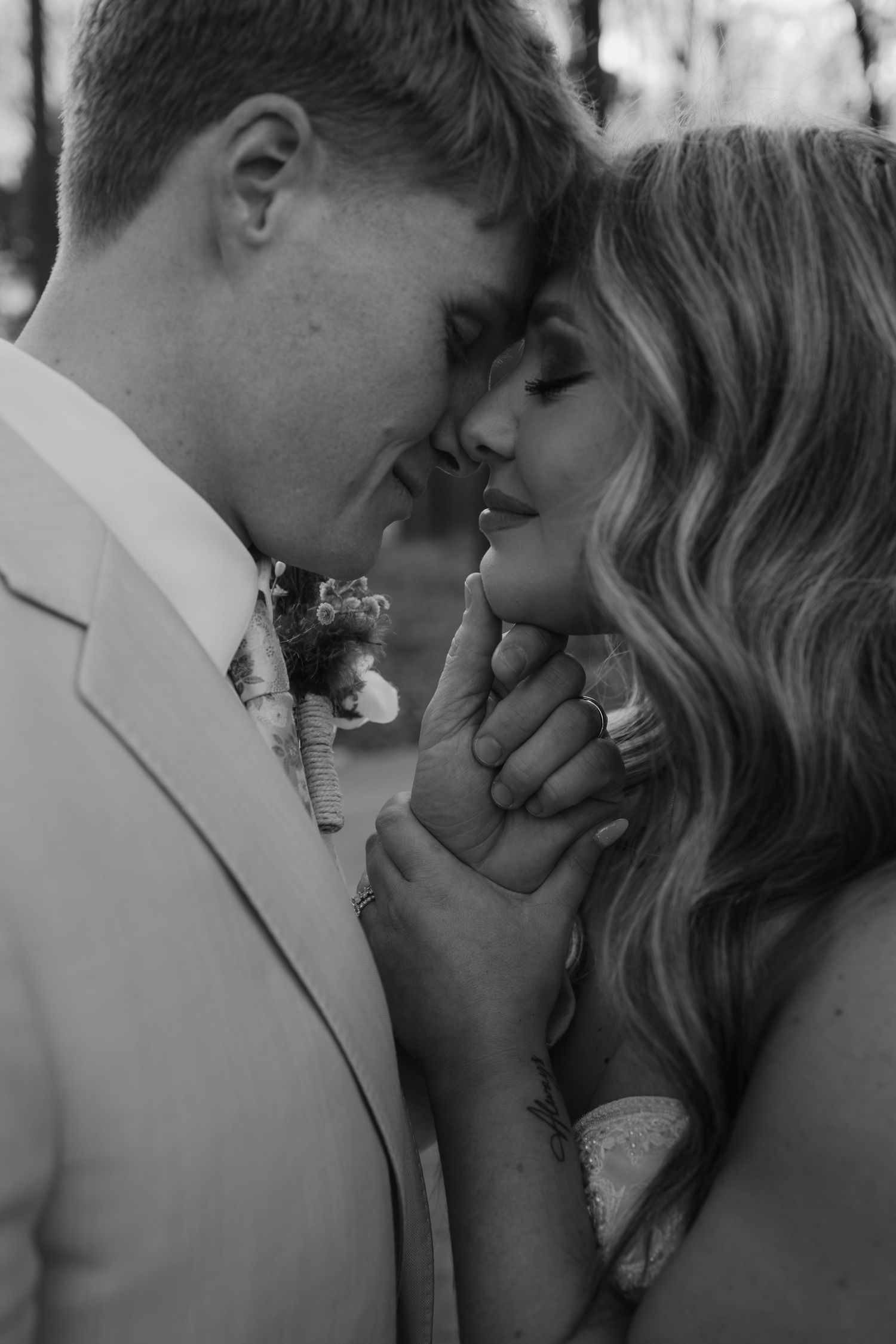 Black and white romantic close-up of bride and groom touching foreheads, hands clasped together tenderly.