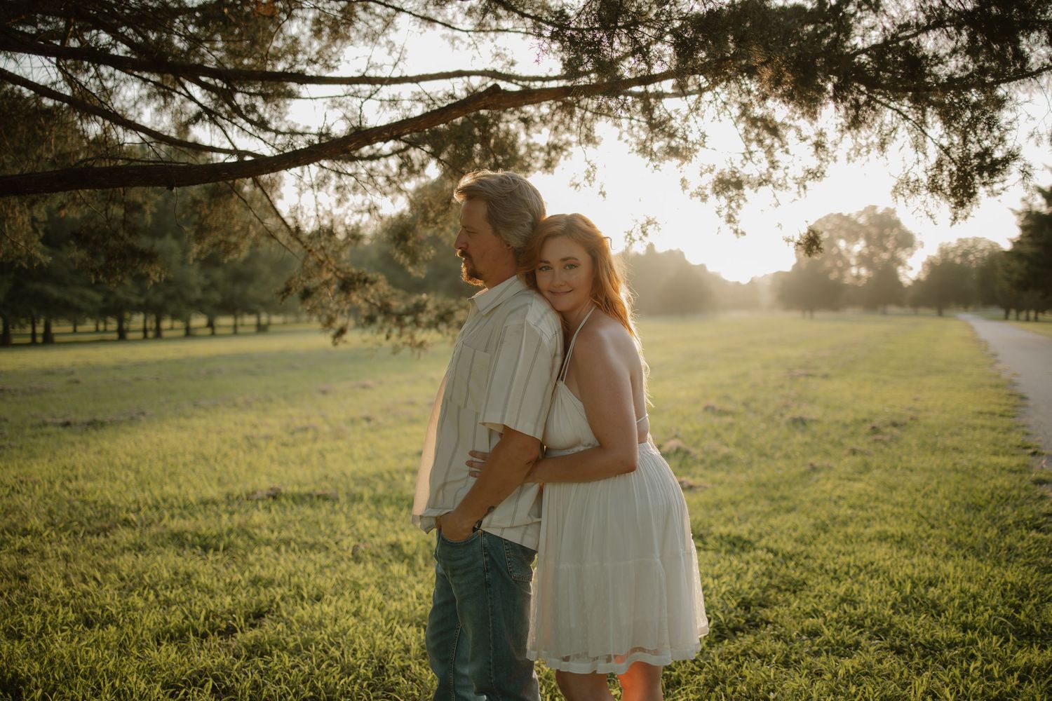 Couple embracing at golden hour in a lush green park, bathed in warm sunset light.