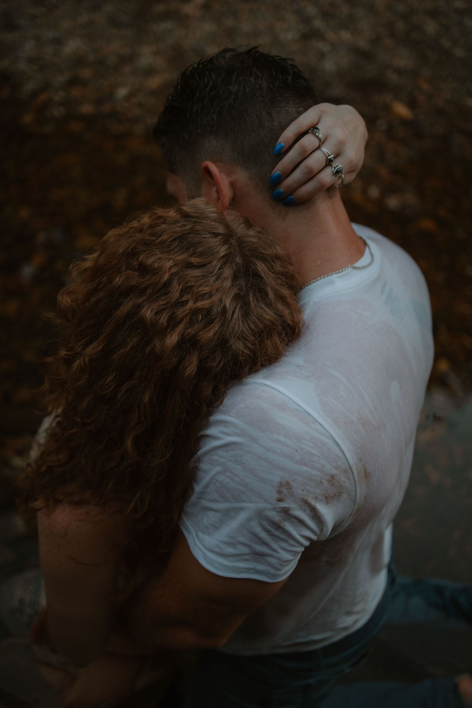 Romantic couple embracing outdoors, woman with curly red hair holding mans neck tenderly.