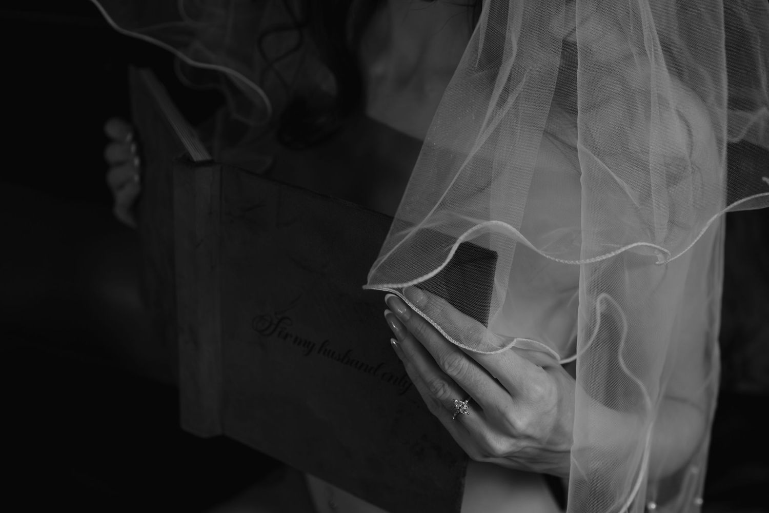 Black and white photo of a bride holding her wedding veil and bouquet.