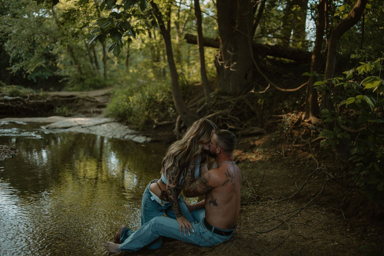 Couple sharing an intimate moment by a serene forest creek, sitting together on the rocky bank.