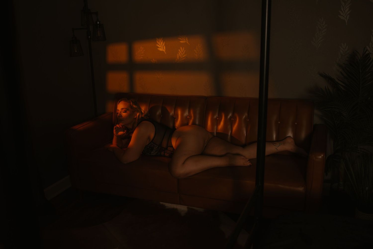 Person resting on a leather sofa in a warmly lit room with amber light casting window shadows.