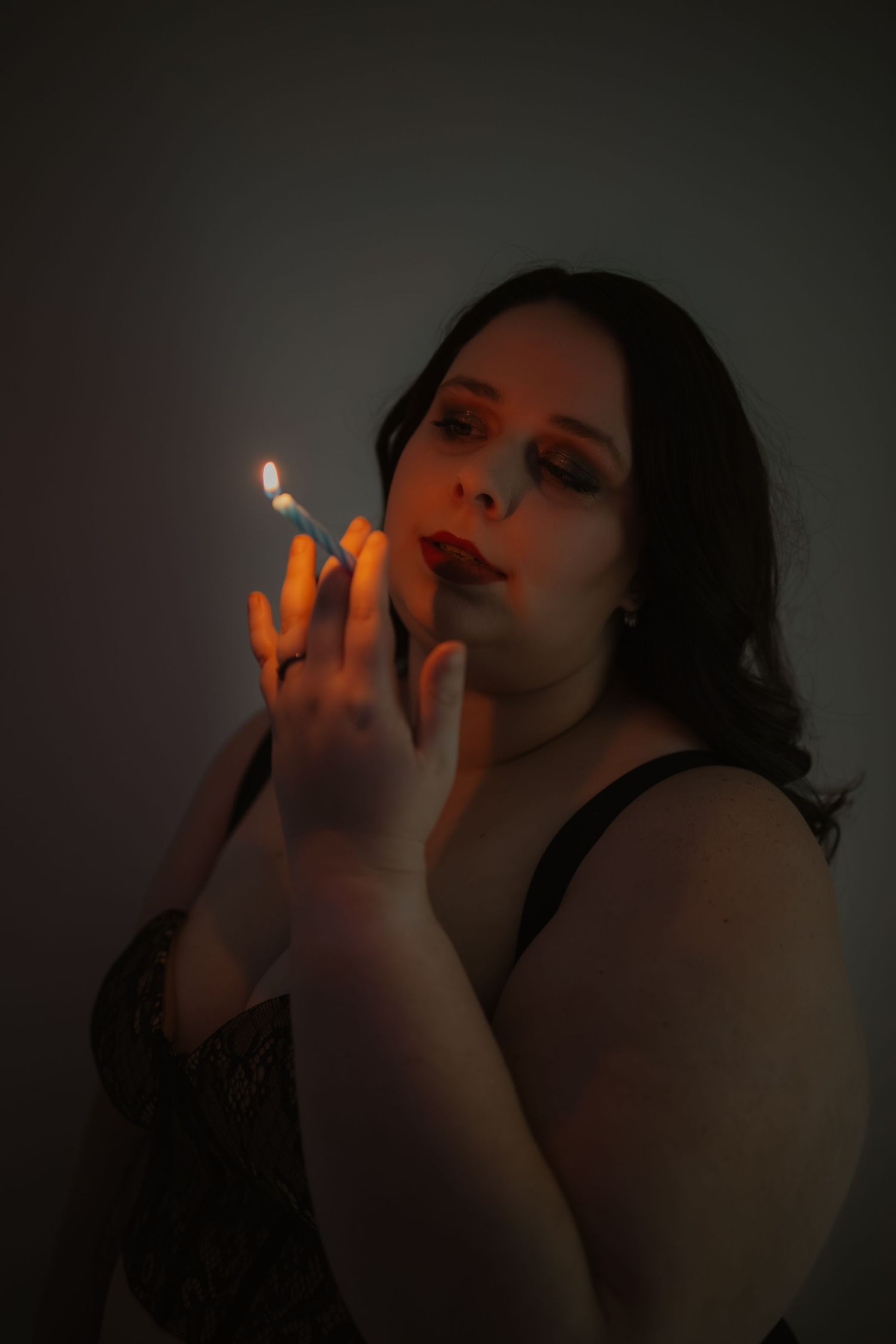 Woman with red lips holding a lit lighter in dramatic low-key moody portrait lighting.