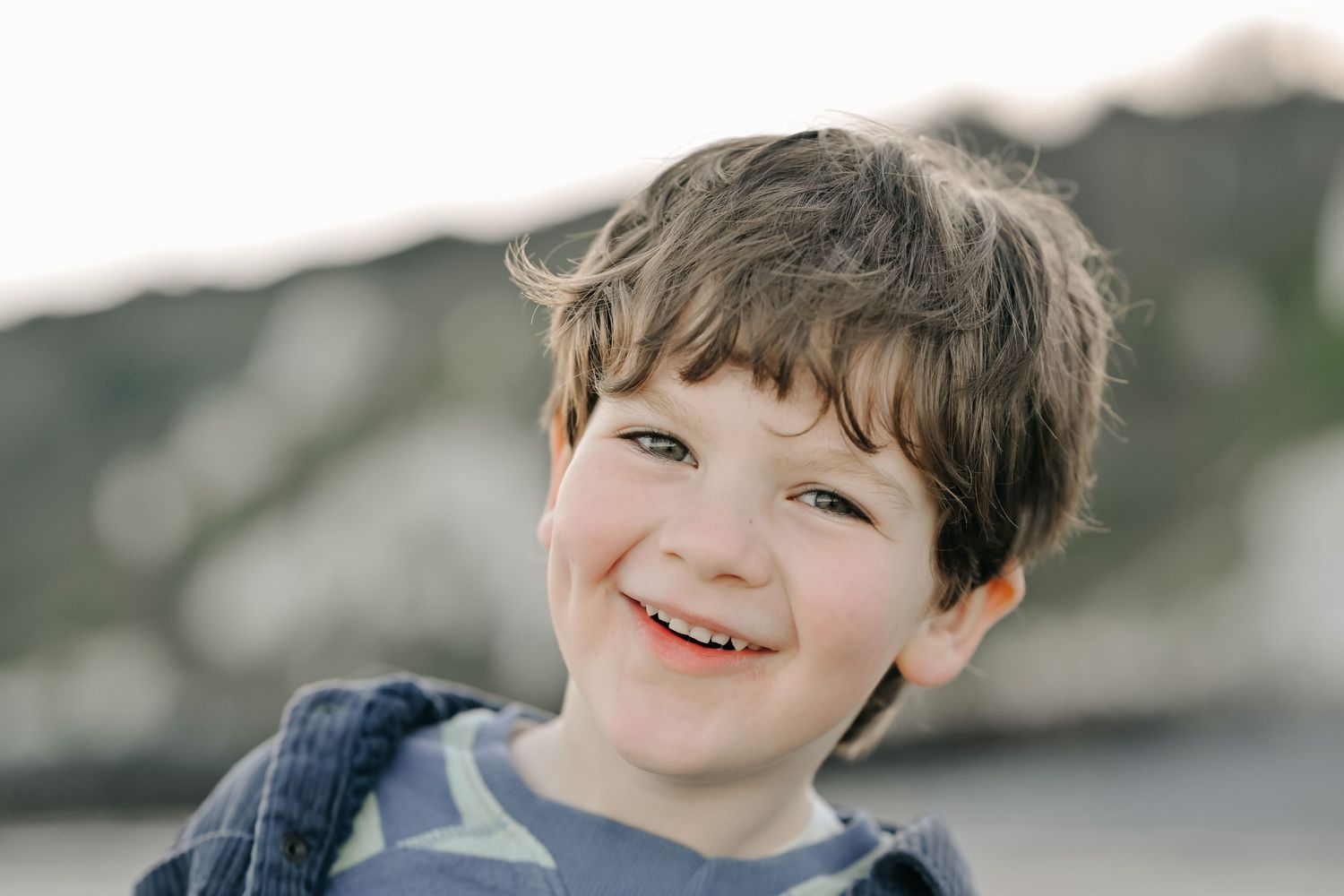Adorable young boy with brown hair smiling warmly at the camera in natural outdoor lighting during a family photoshoot in Eastbourne, Sussex