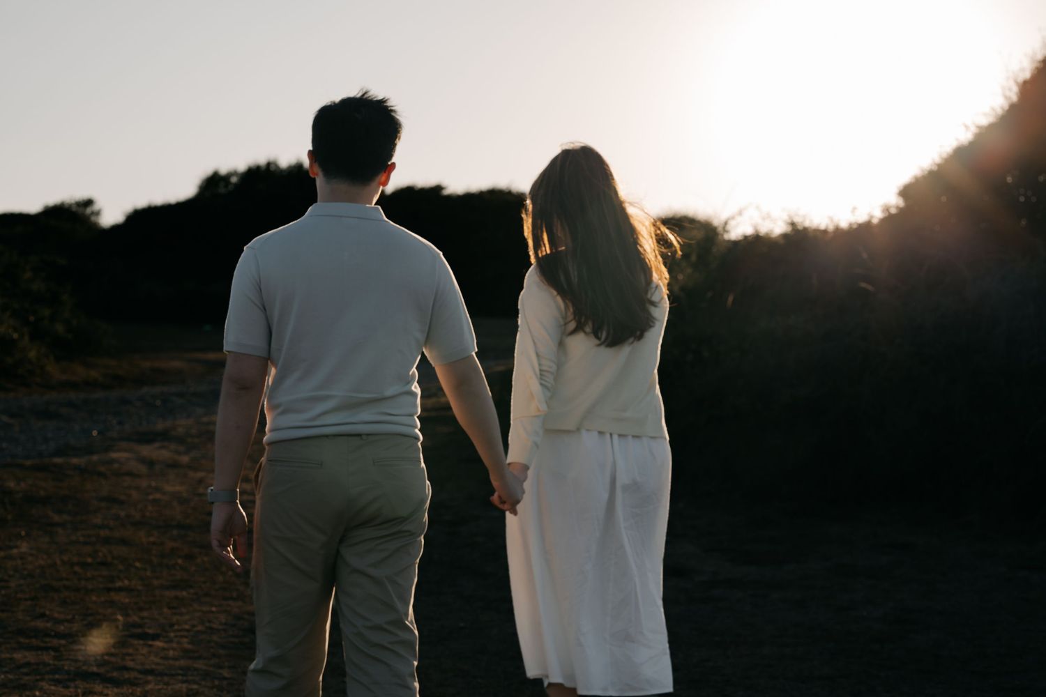 Couple holding hands walking toward sunset in a romantic outdoor setting.