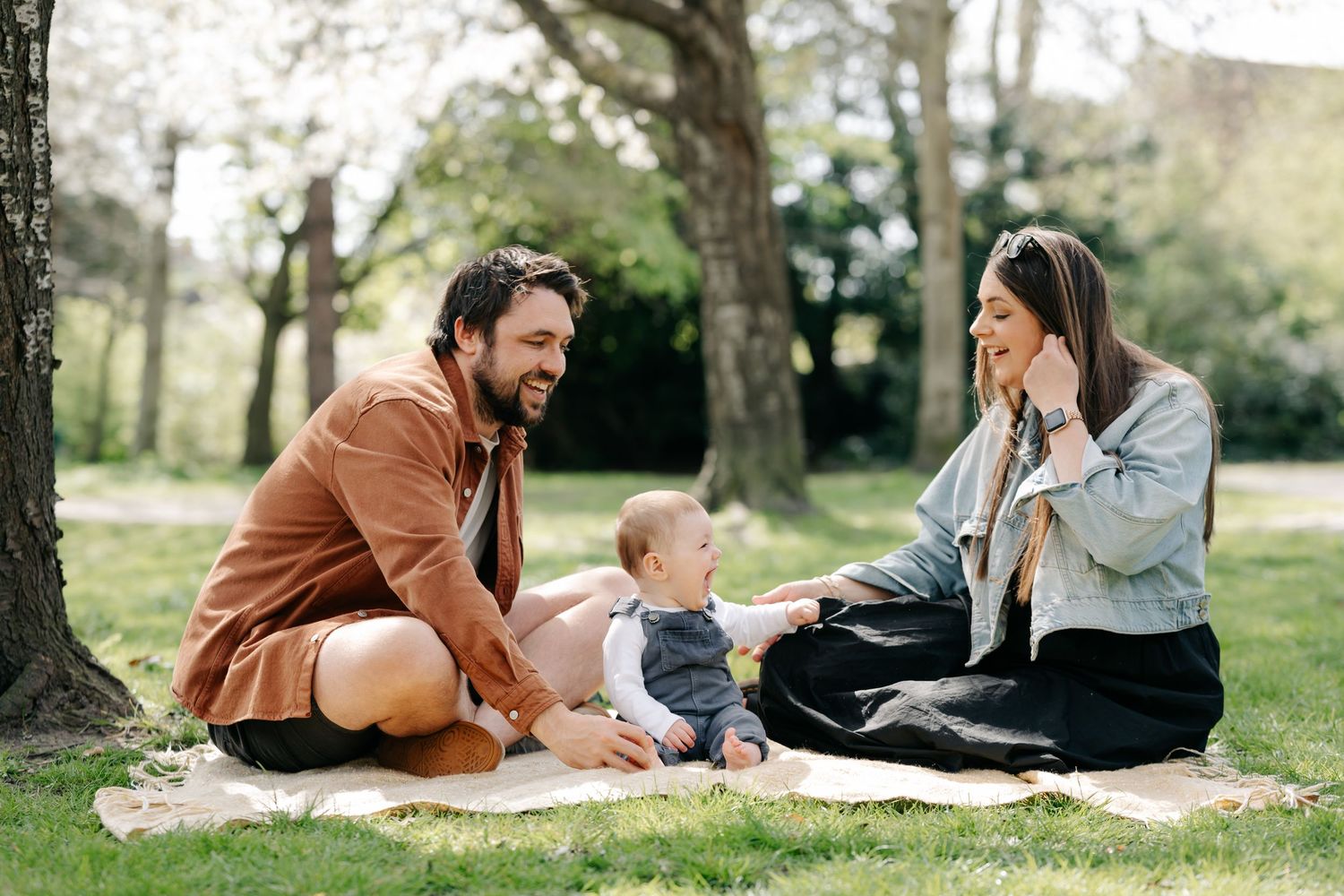 Happy family with baby enjoying a sunny picnic on a blanket in a lush green park, during a family photography portrait session in Eastbourne