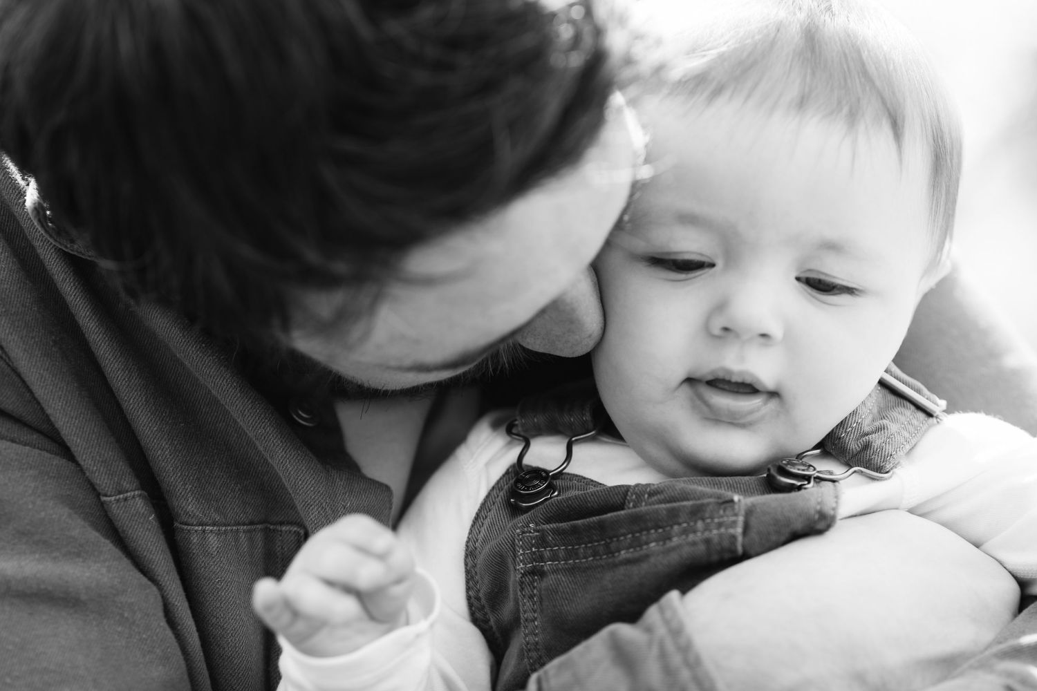 Tender black and white portrait of a father gently kissing his baby on the cheek. During a father and baby photoshoot in eastbourne Sussex