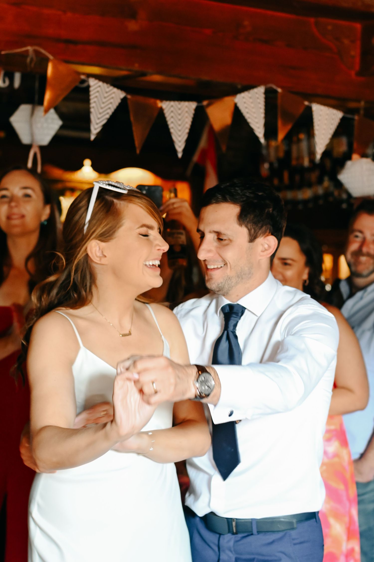 Bride and groom share their first dance, smiling joyfully, with wedding bunting decorations in the background in wedding in a pub Sussex