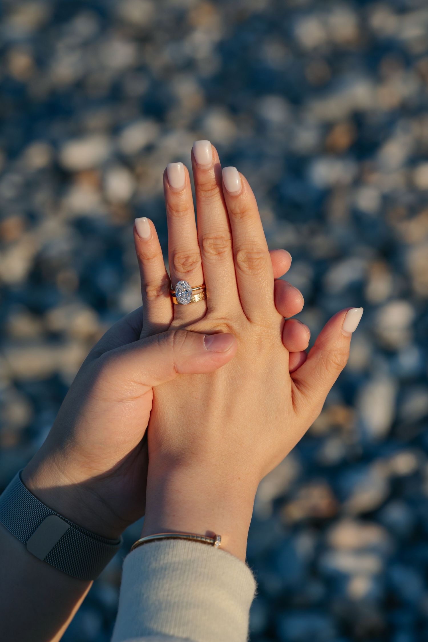 Close-up of an engagement ring with a diamond on a womans hand over a pebble beach background.