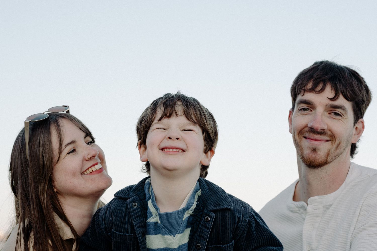 Happy family of three smiling together against a clear sky, parents flanking their young son, family photoshoot on eastbourne beach