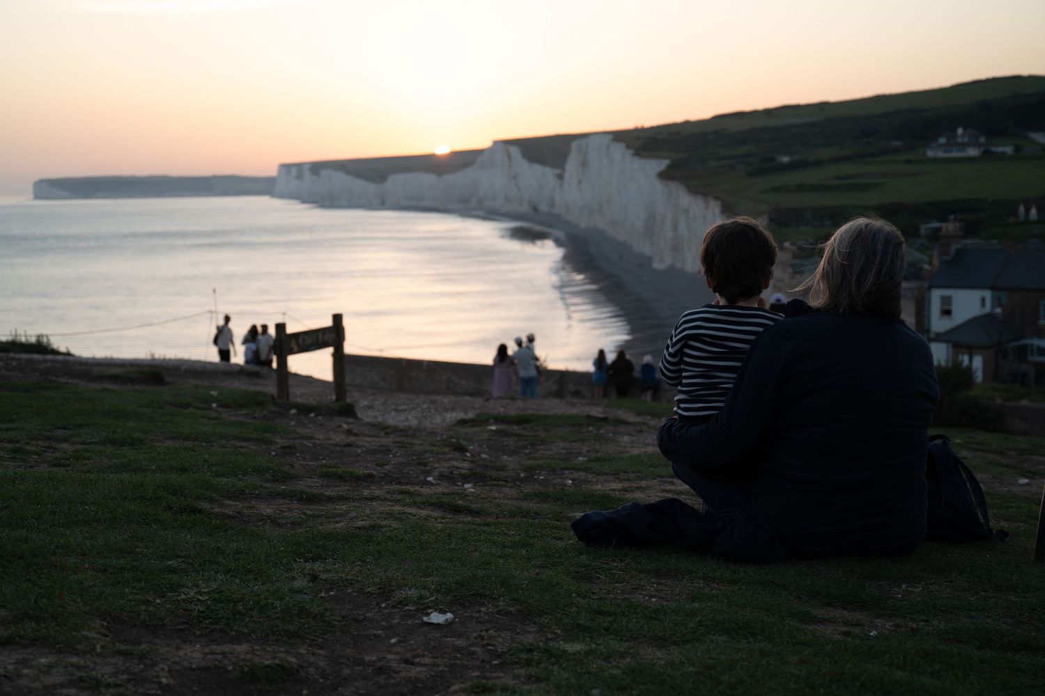 Couple sitting on cliffs at sunset overlooking white chalk coastline and calm sea in golden evening light, portrait session, Eastbourne.