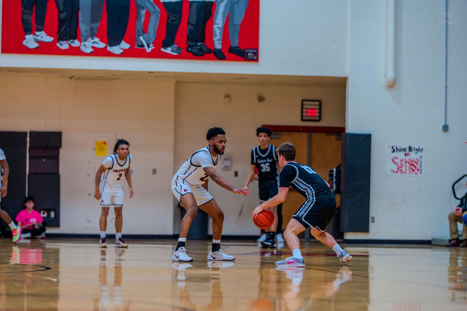 High school basketball players compete on the court as player in white dribbles against black-uniformed defender.