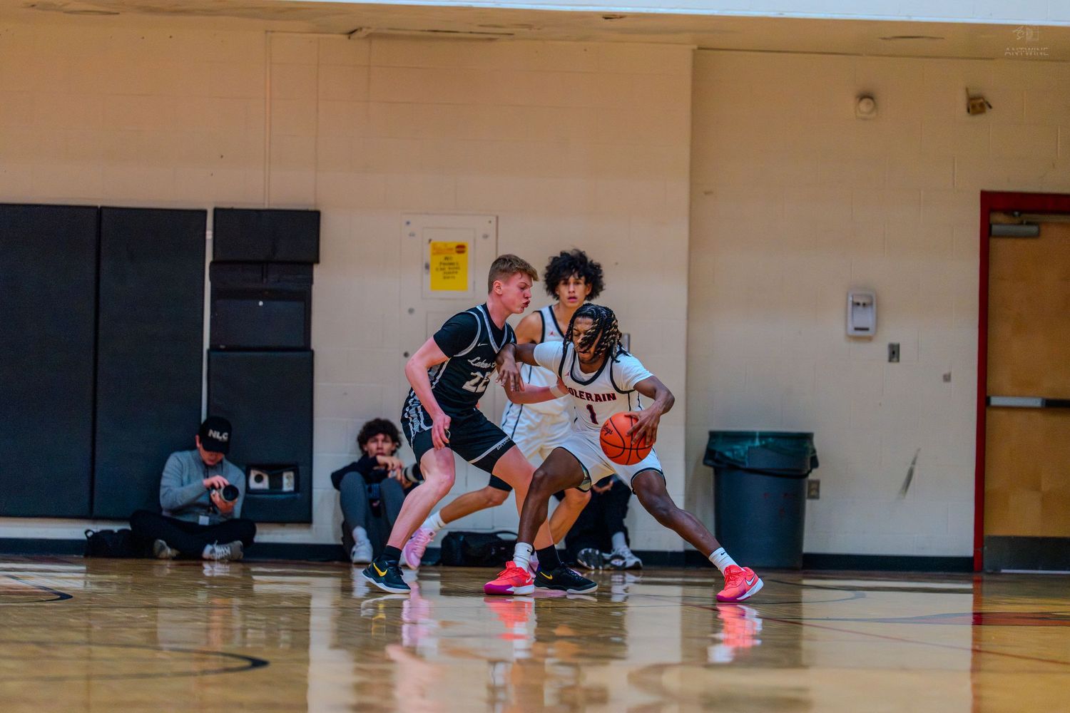 Basketball player protects the ball while being double-teamed by two defenders during a high school game.