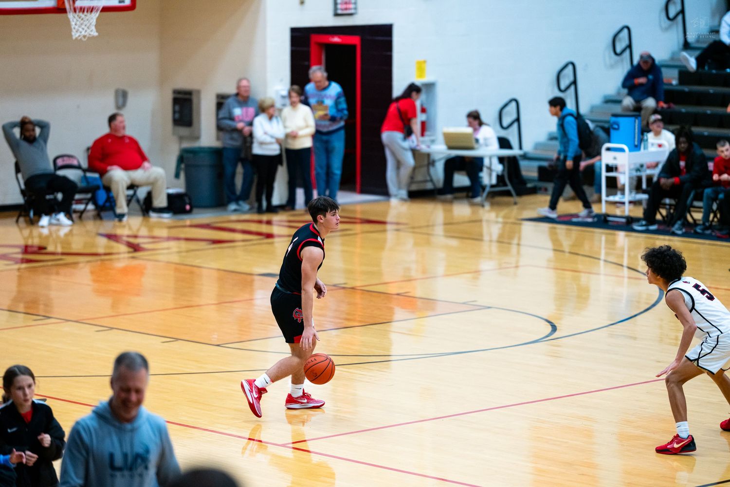 Basketball player in black uniform dribbles ball during high school game with fans watching.