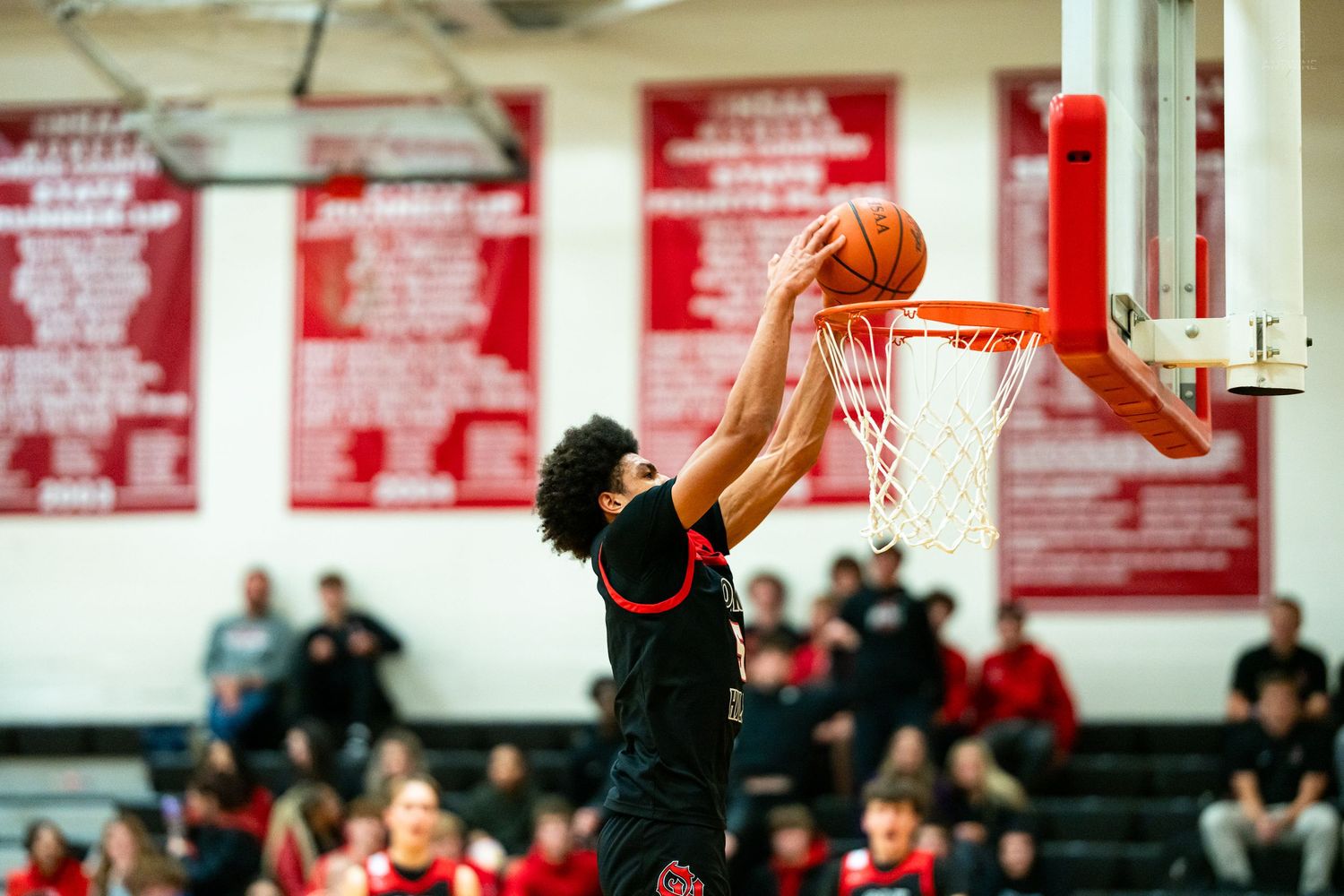 High school basketball player in black and red uniform attempts a layup at an indoor gymnasium hoop.