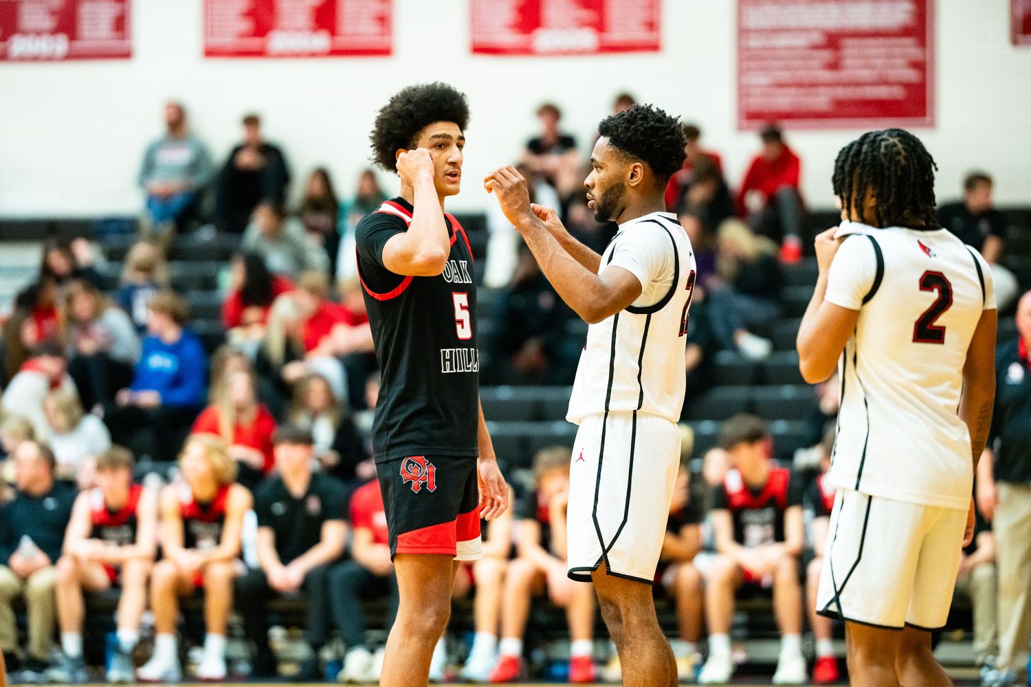 Two high school basketball players in red and white uniforms exchange high five during game.