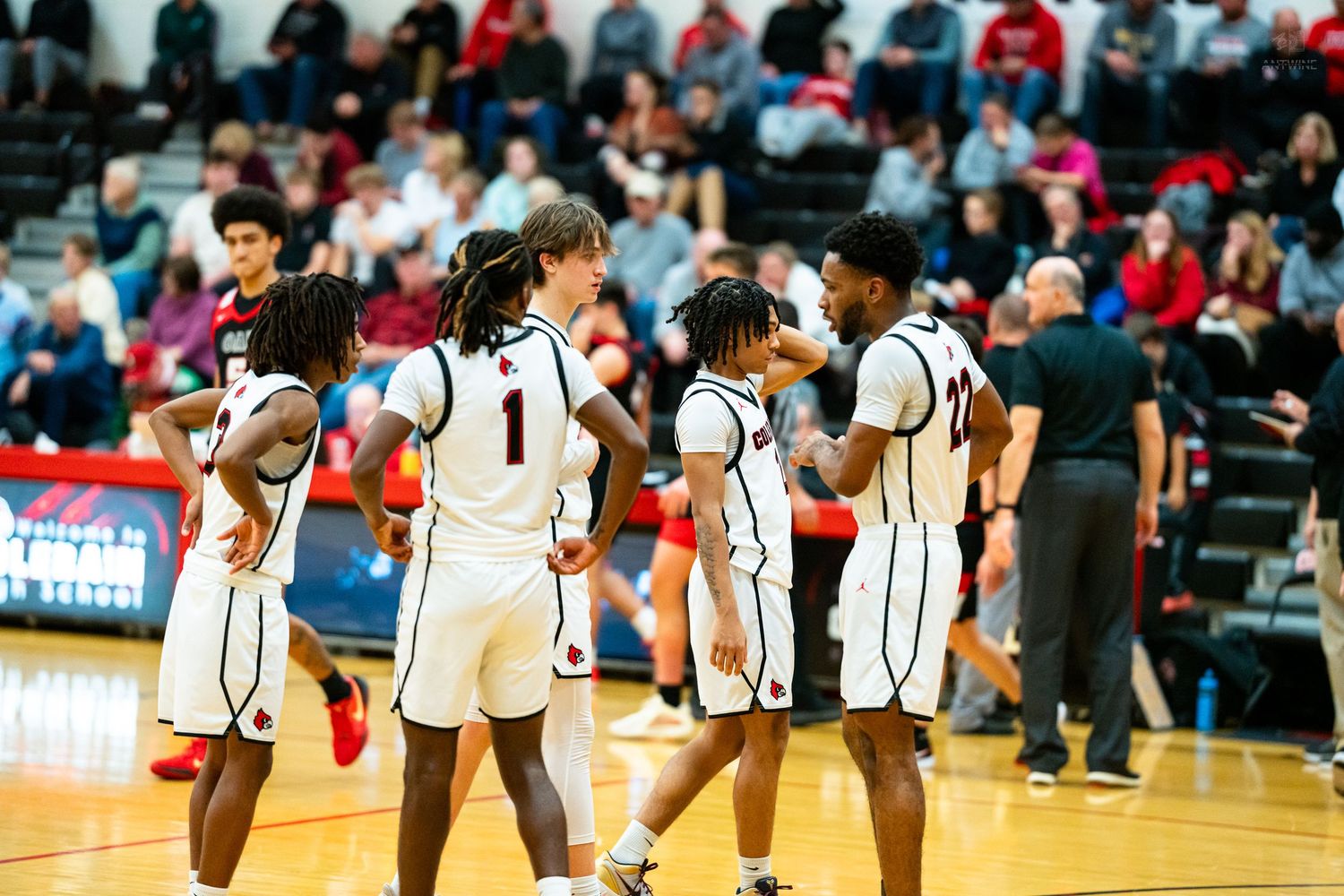 High school basketball players in white uniforms walk together on the court during a basketball game.