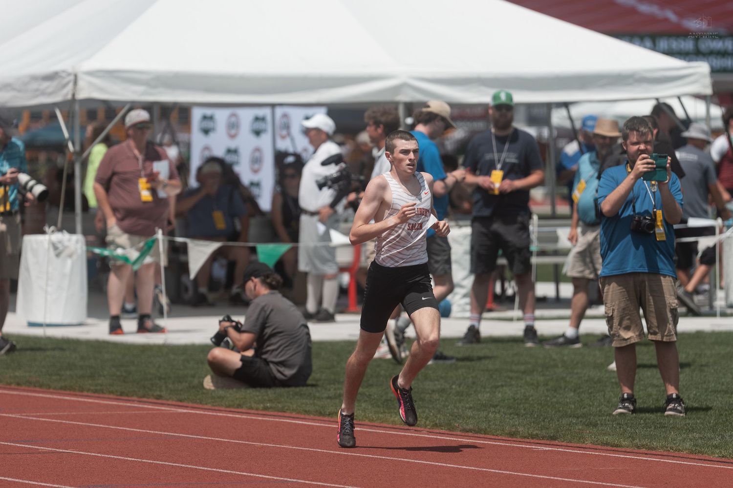 Male athlete running on red track at outdoor NCAA track and field championship meet with spectators watching.