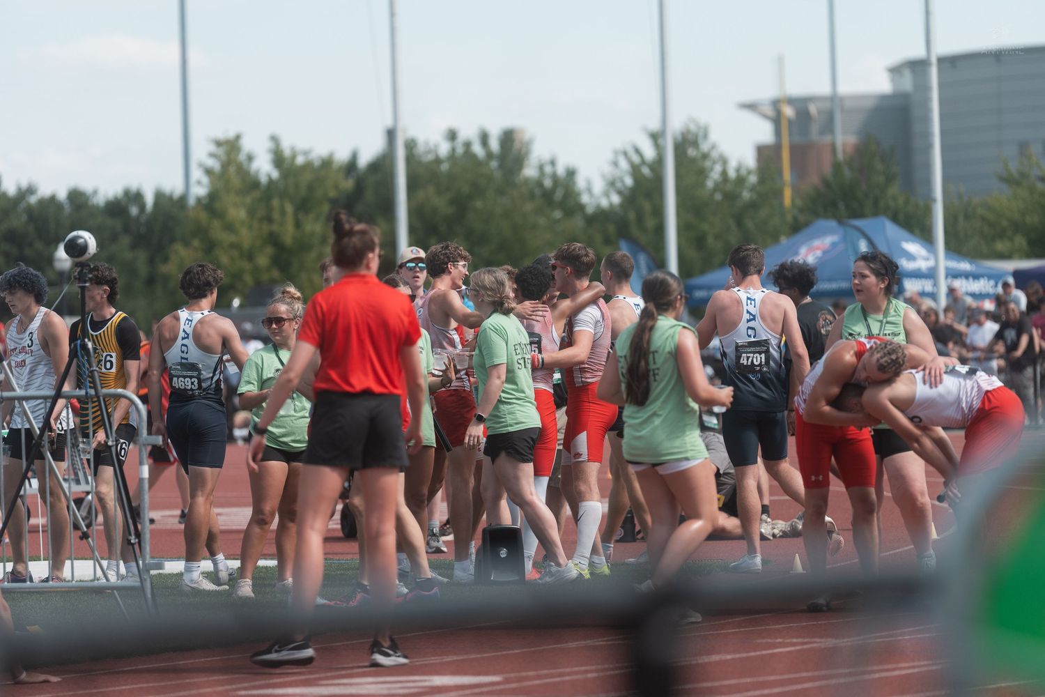 Track and field competitors in green and red uniforms congregating on the track between events.