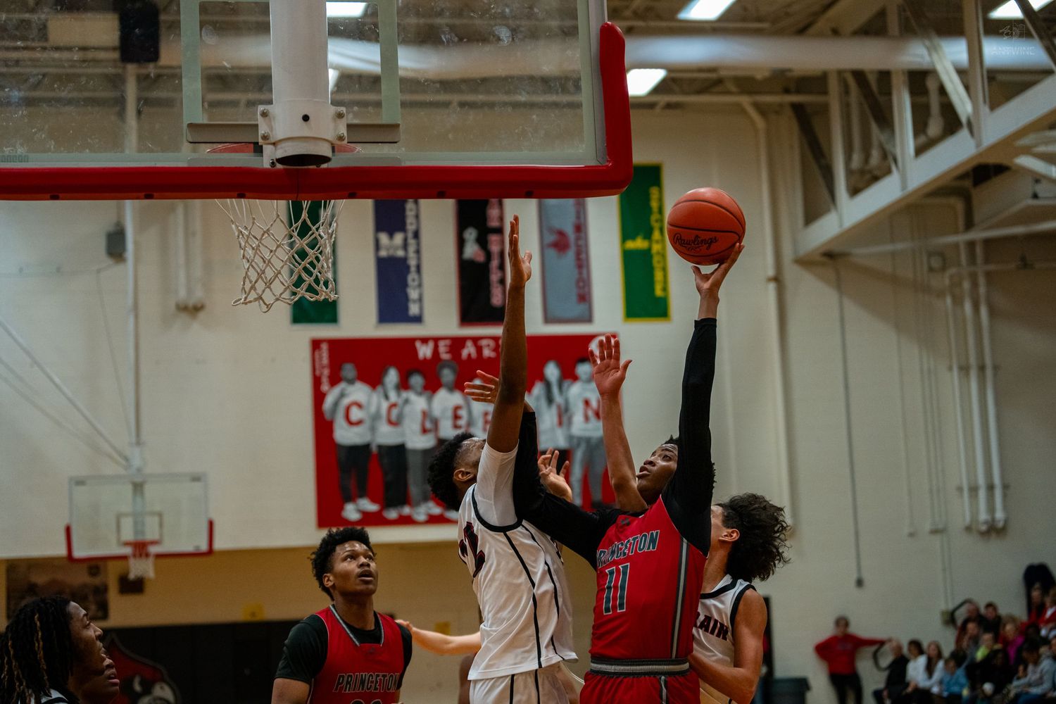 Basketball player in red attempts a layup over a defender during a high school basketball game.