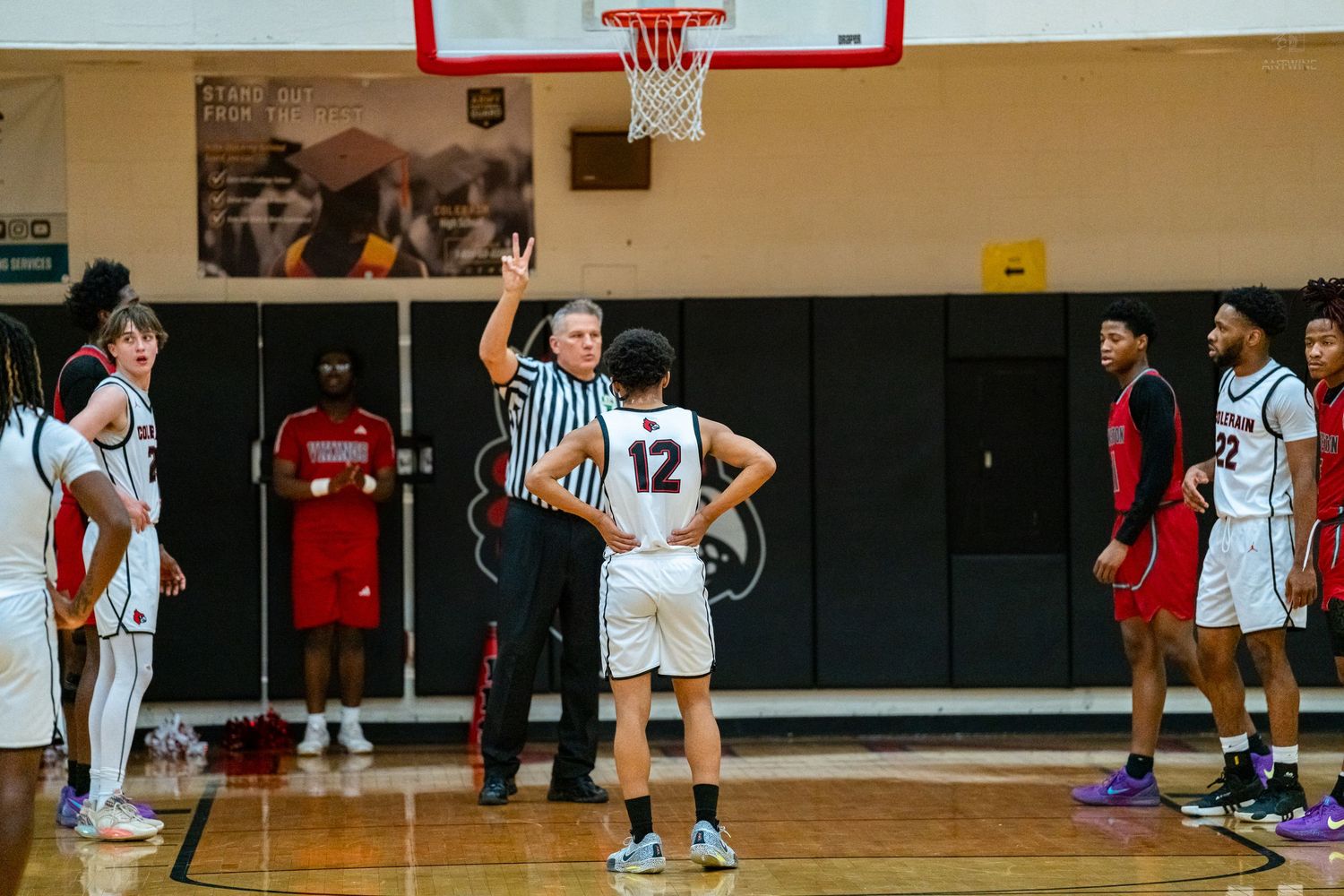 A referee signals during a high school basketball free throw with players lined up on both sides.