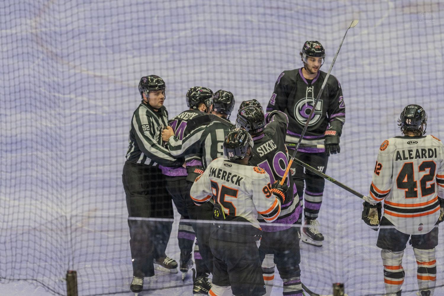 Hockey referee separates players from two teams during a tense moment near the boards.