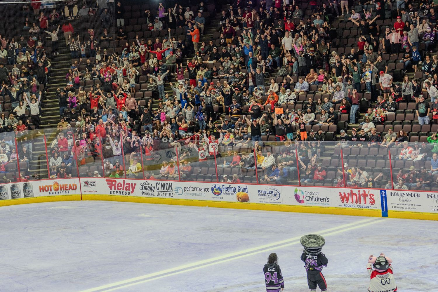 Packed hockey arena crowd cheering as mascot performs on the ice rink.