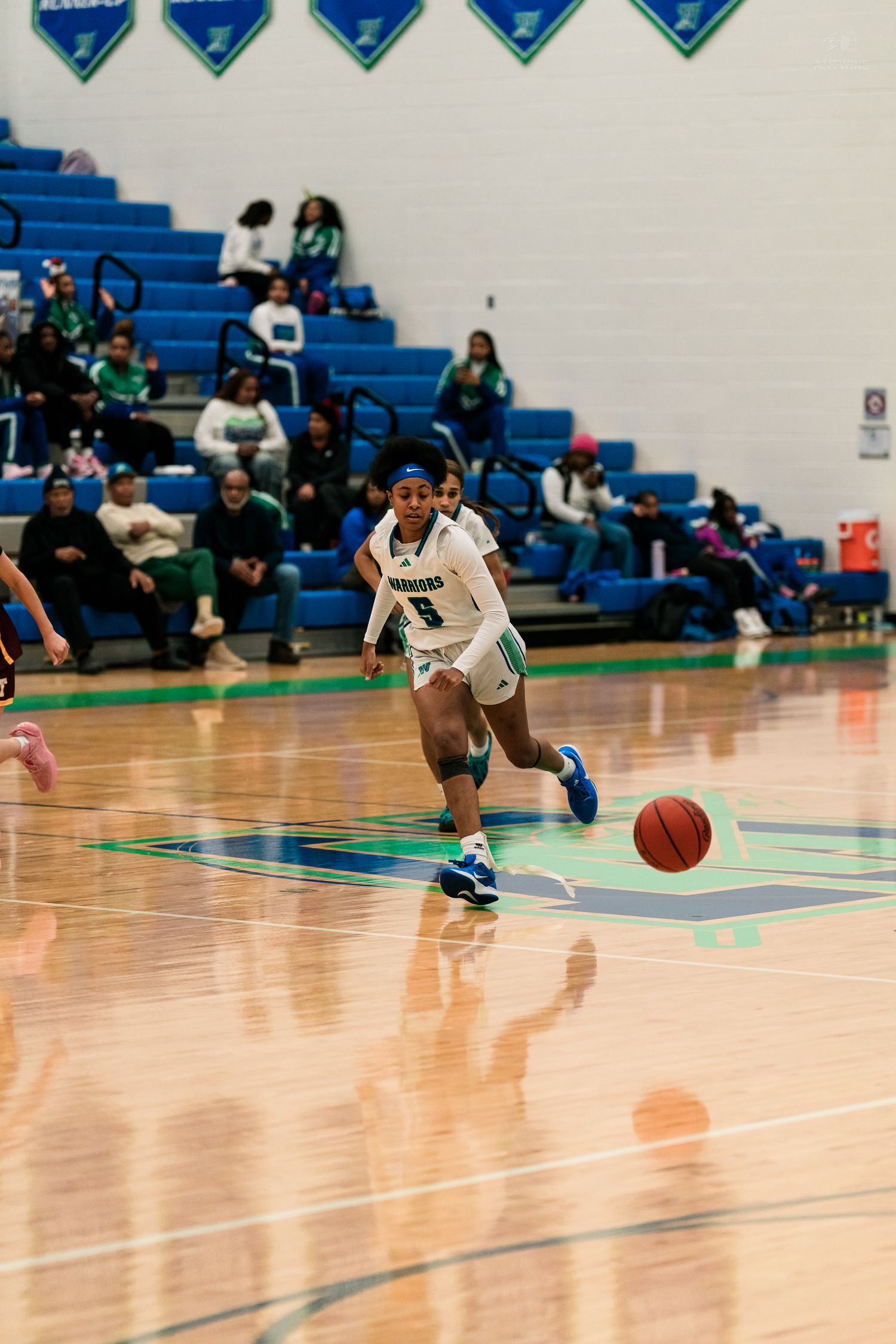 A female basketball player in teal dribbles down the court during a high school girls basketball game.