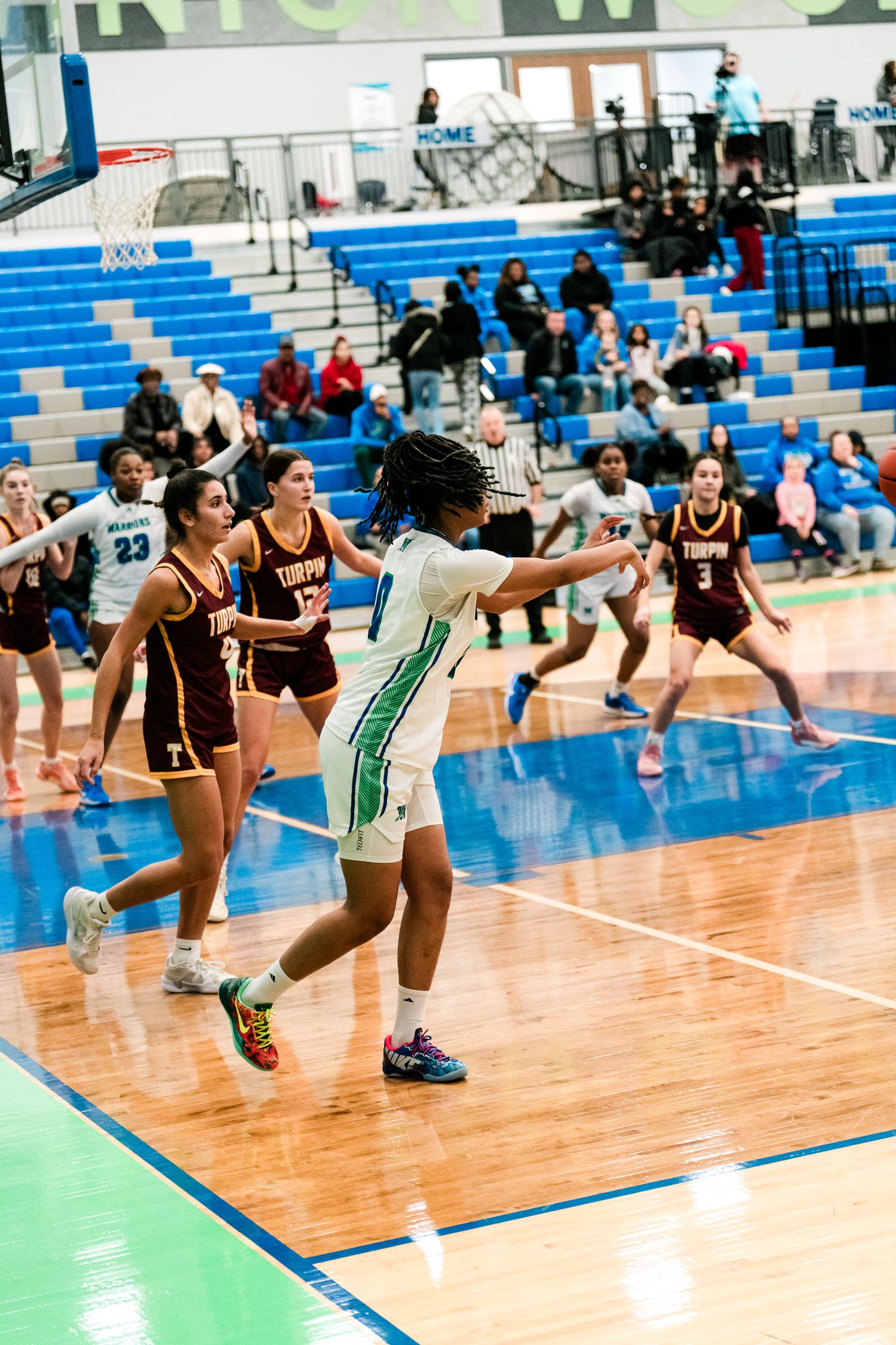 Female basketball player in white Warriors jersey passes ball while surrounded by Turpin players in maroon uniforms.