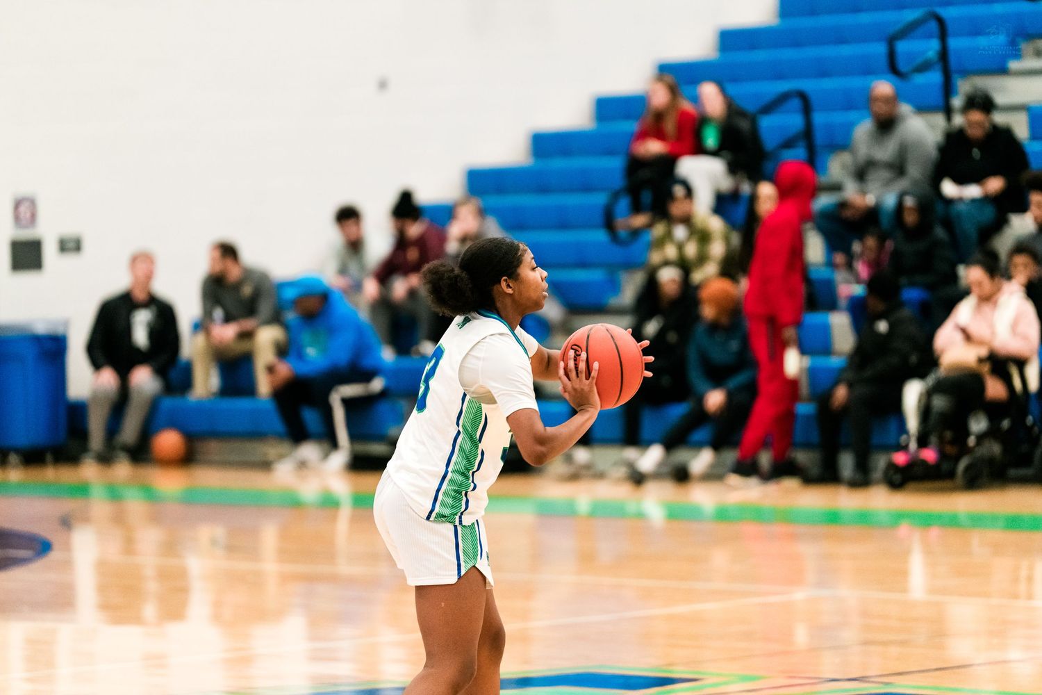 Warriors girls basketball player shoots from outside during high school game with fans watching.
