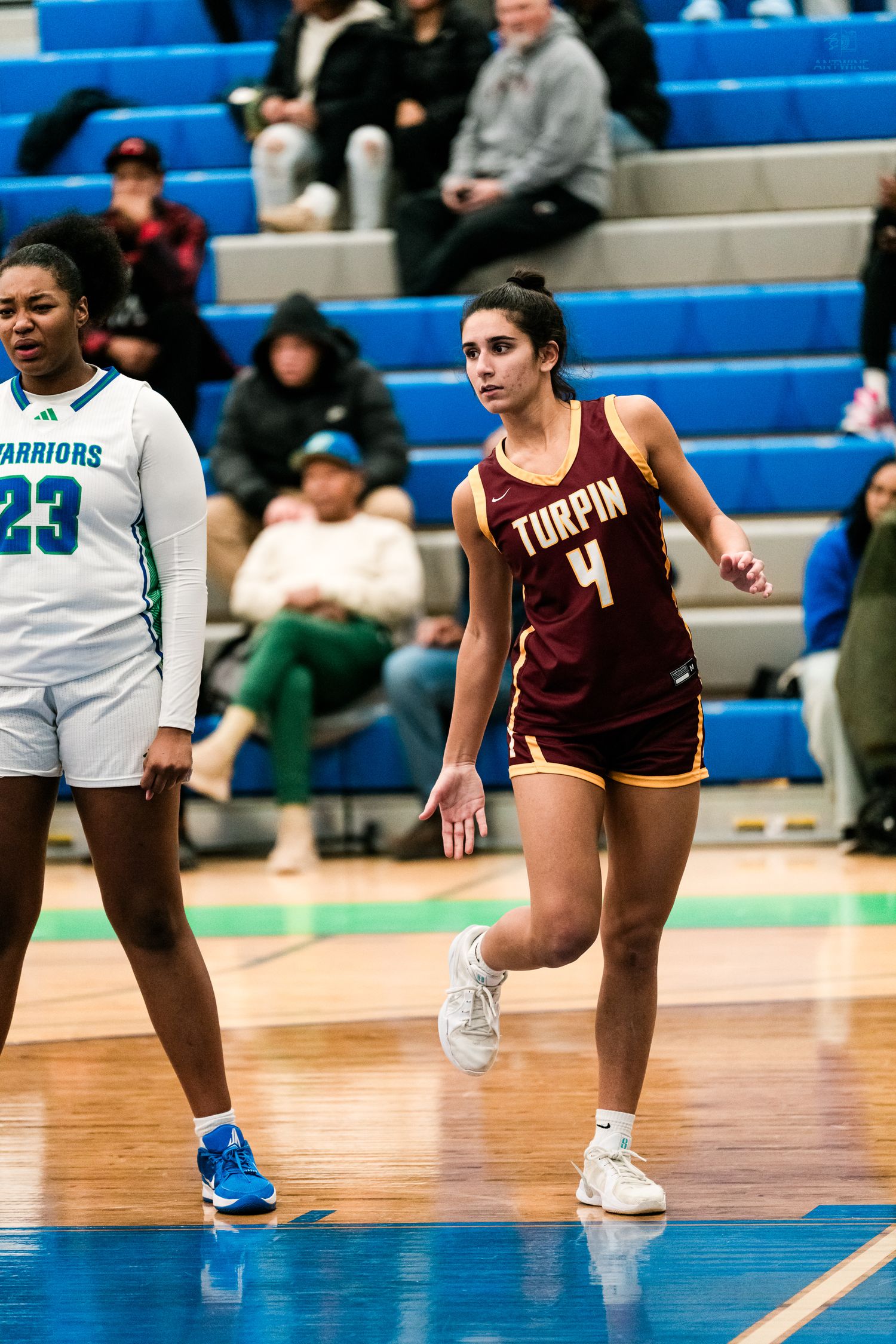 Turpin High School female basketball player number 4 runs on court alongside a Warriors player during an indoor game.