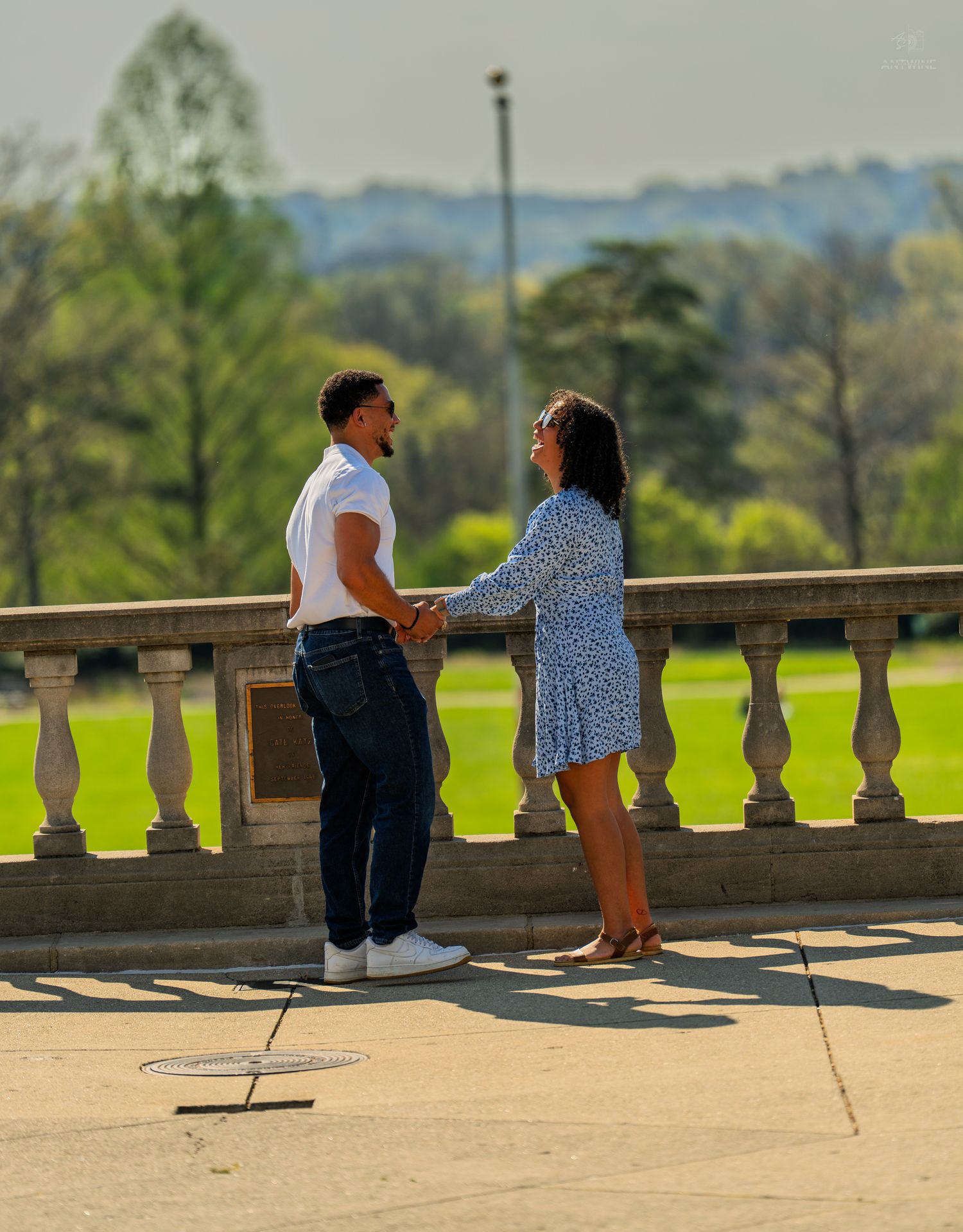Young couple sharing a romantic moment holding hands on a classic stone balcony in a park.