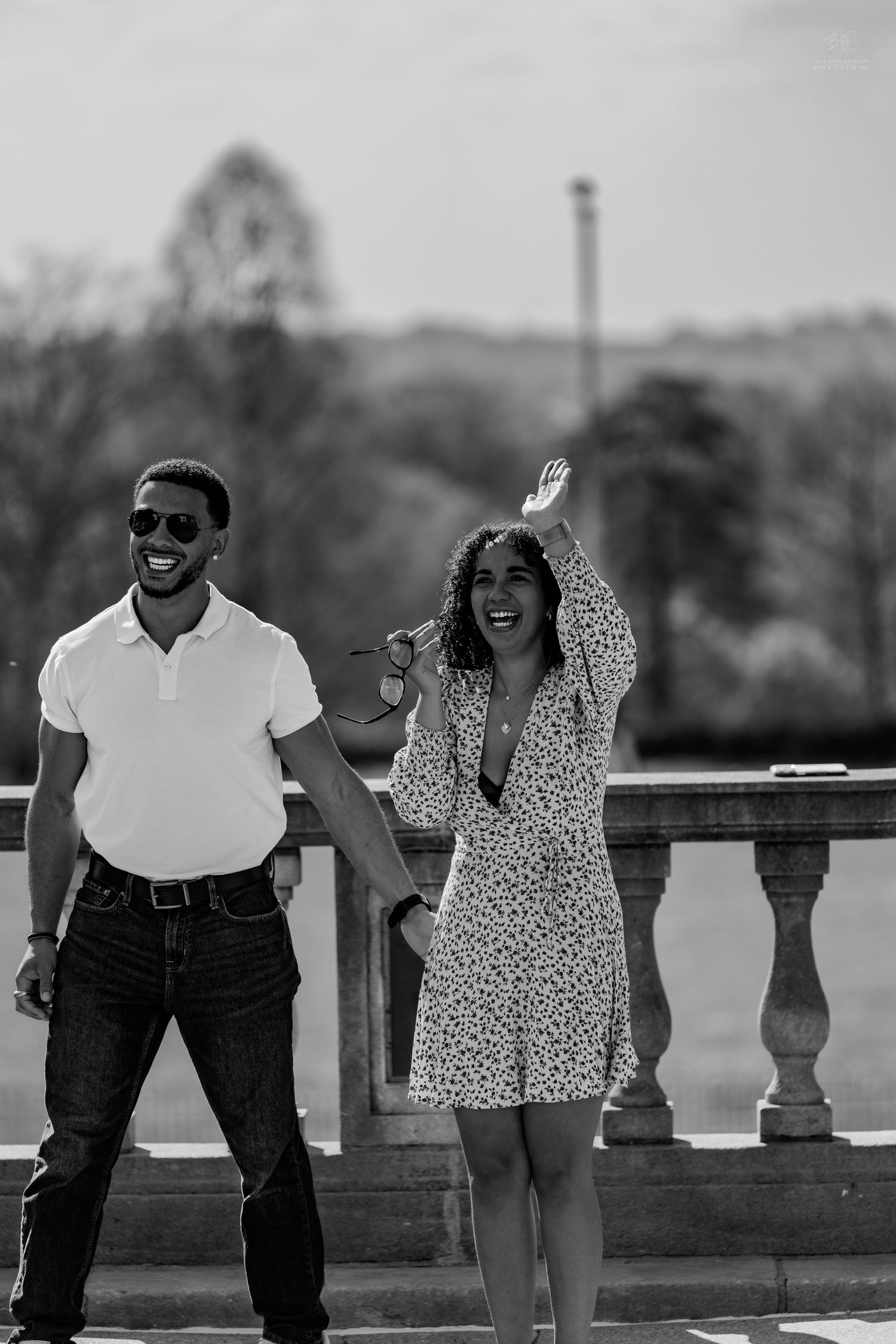 Black and white photo of a joyful couple on a stone terrace, woman waving hand in the air.