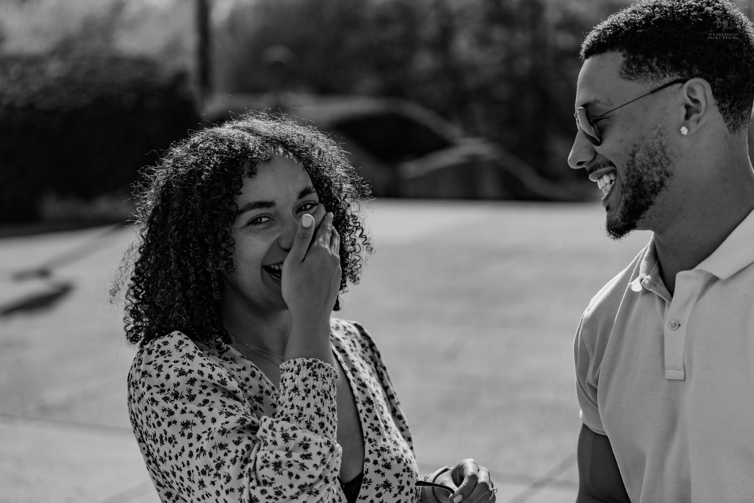 Black and white photo of a joyful couple laughing together outdoors during a surprise proposal moment.
