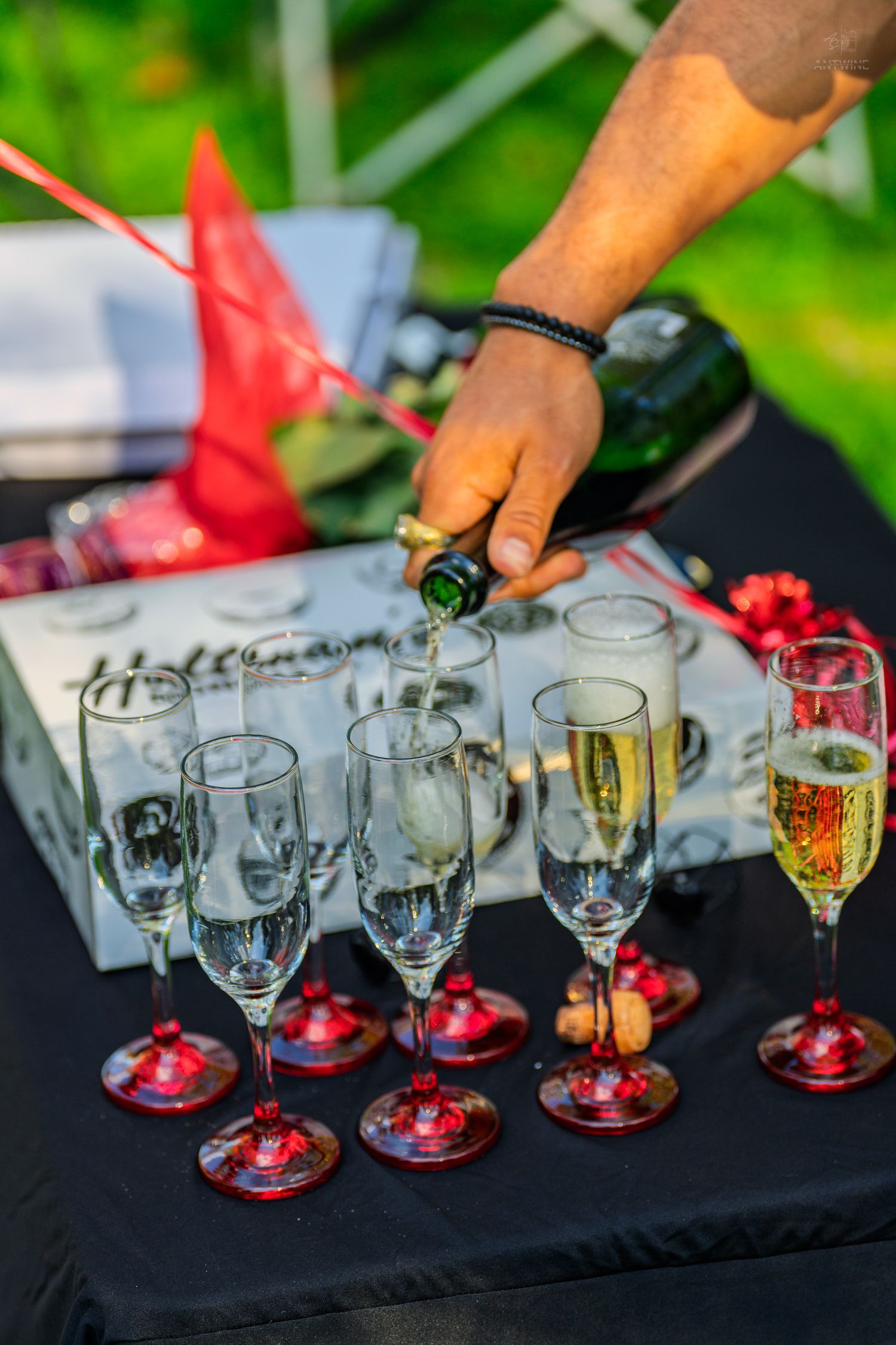Hand pouring champagne into elegant flutes arranged on black table at outdoor celebration.