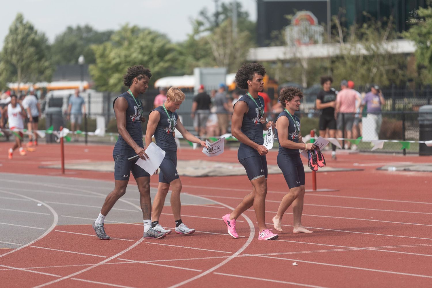 Four track athletes walk along a red track after completing a relay race at a meet.