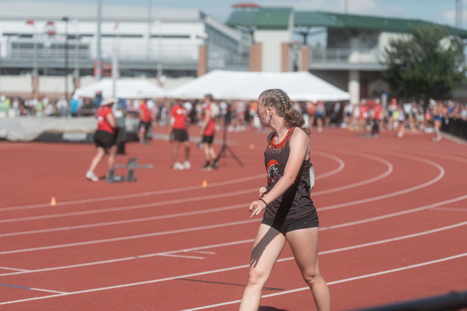 Young female track athlete walks on a red track during an outdoor track and field competition.
