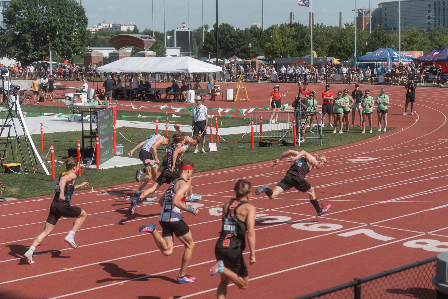 Student athletes compete in a sprint relay race on a red outdoor track at a high school track meet.