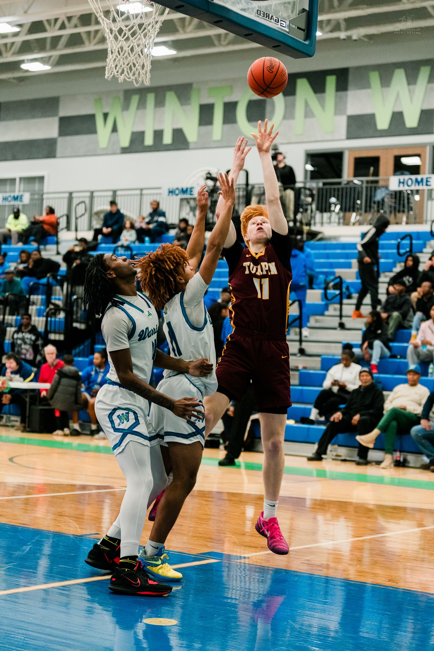 Player #11 in maroon shoots over two Winton Woods defenders in a high school basketball game.