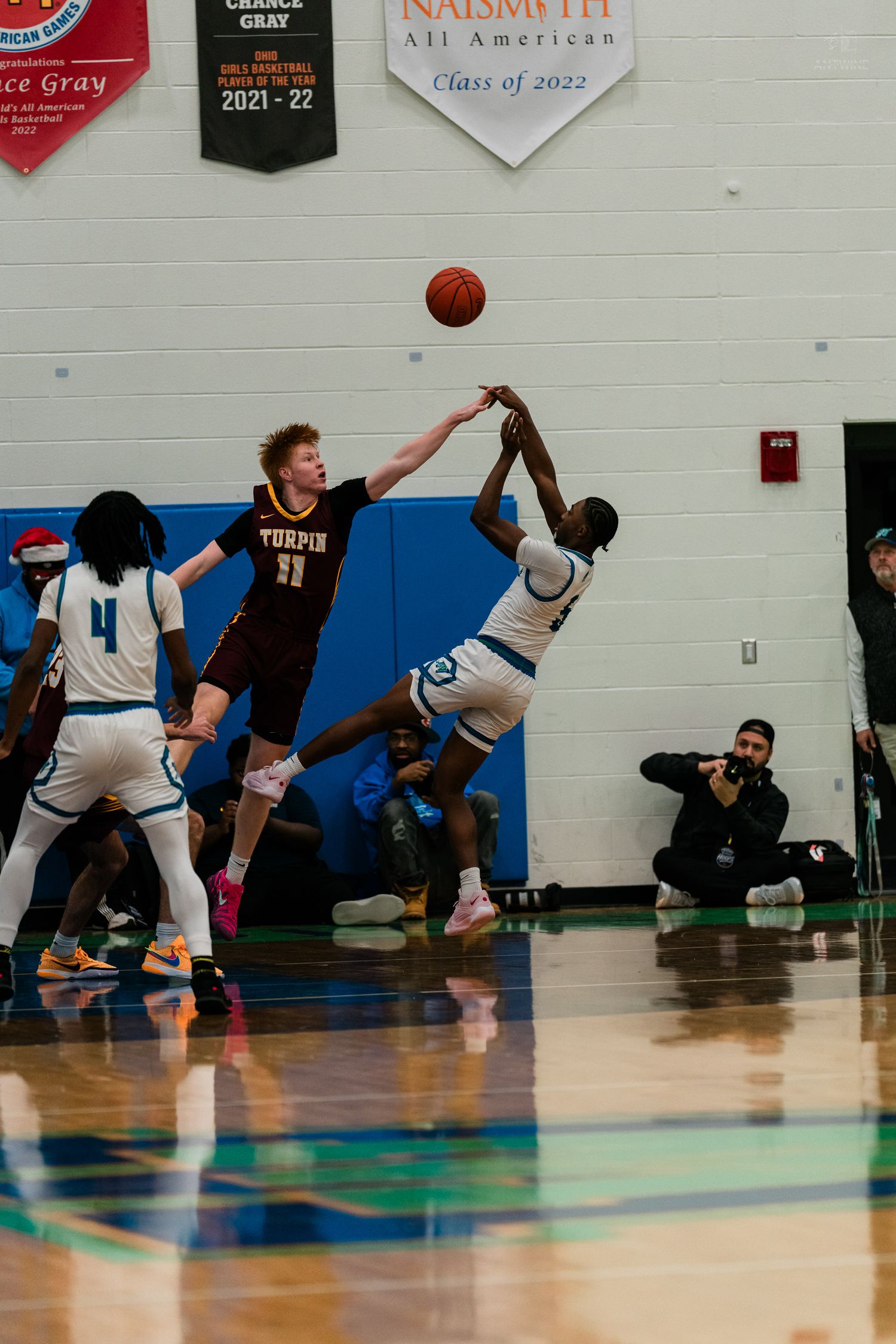 Turpin player contests a shot attempt during a high school basketball game near a Naismith All American banner.