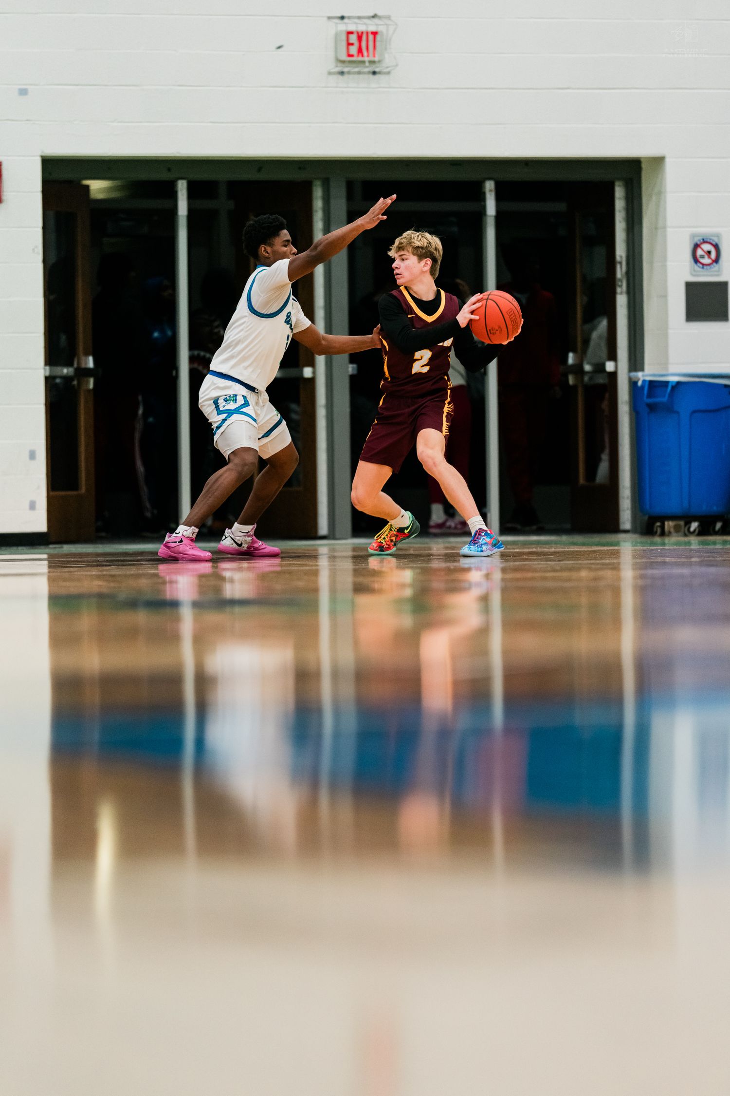 High school basketball player in maroon dribbles past a defender in white during an indoor game.