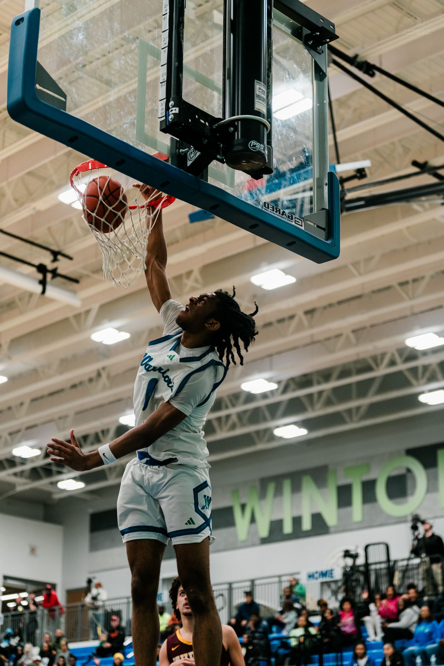A player in white uniform executes a powerful slam dunk during a high school basketball game.