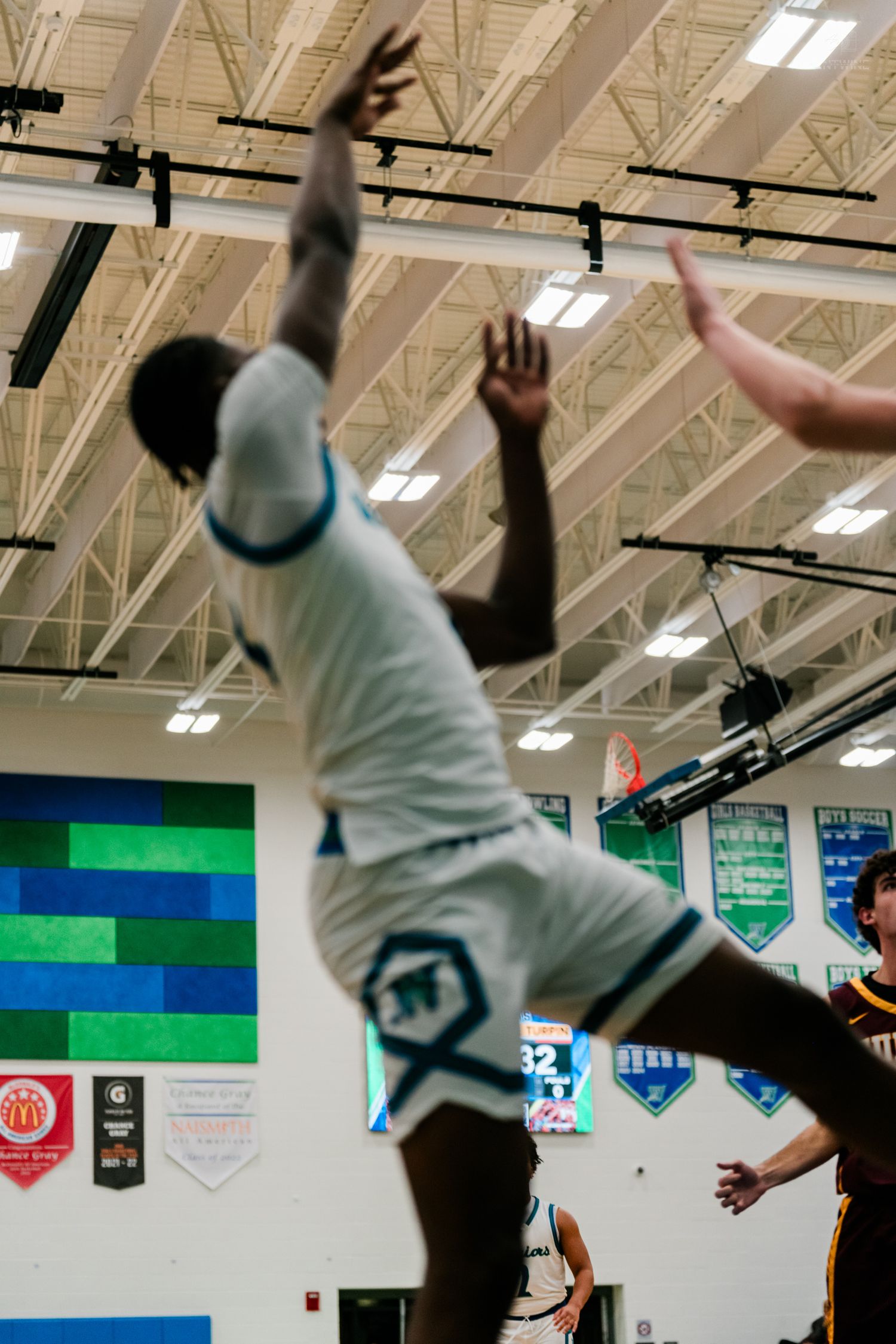 A player in white uniform leaps with arms raised to block a shot during a high school basketball game indoors.