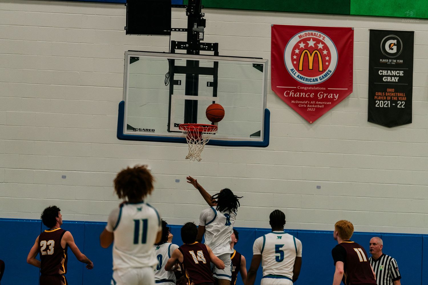 Basketball player attempts a layup during a high school game under a McDonald's championship banner.